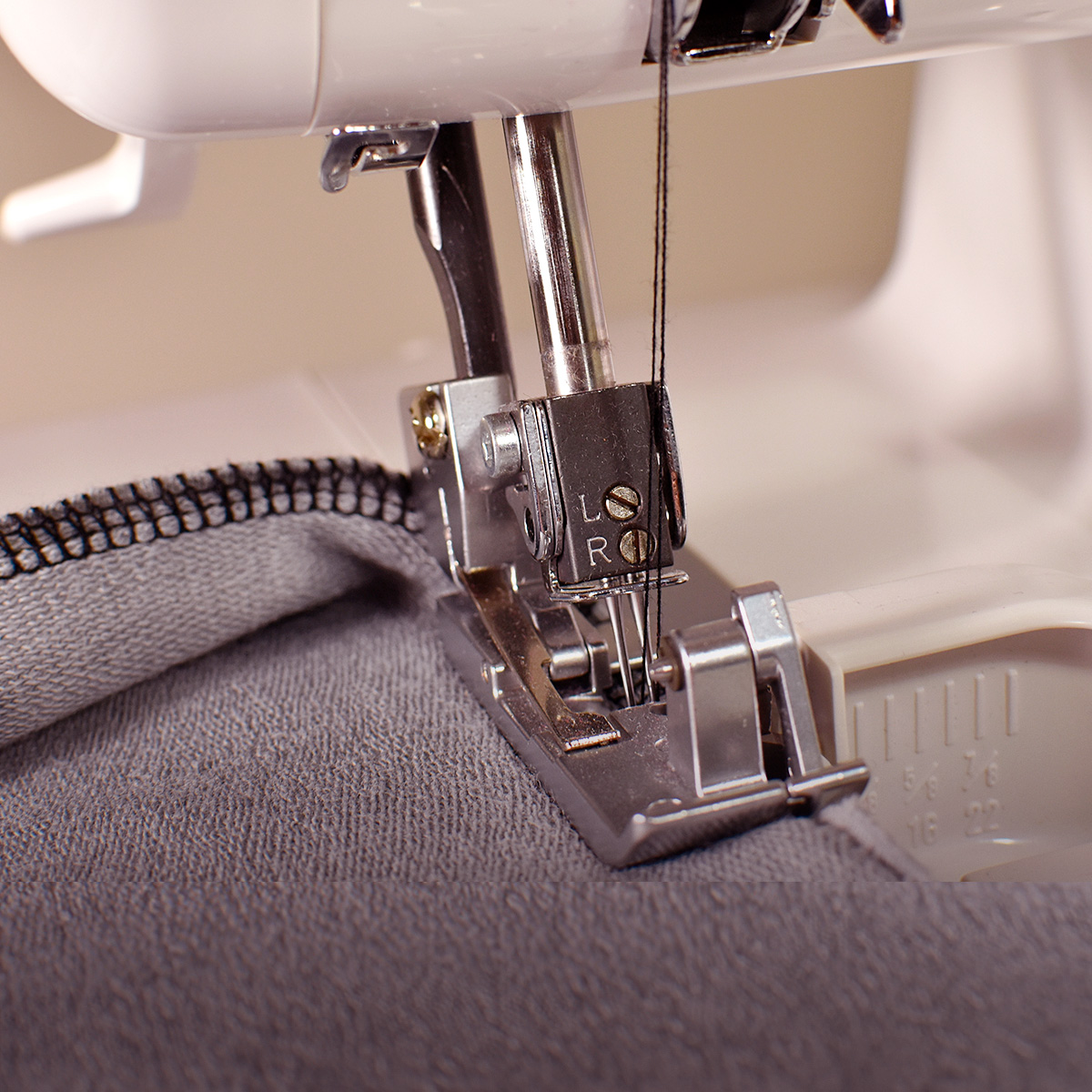 Aguja de máquina de coser con hilo, tela gris. La máquina es blanca.