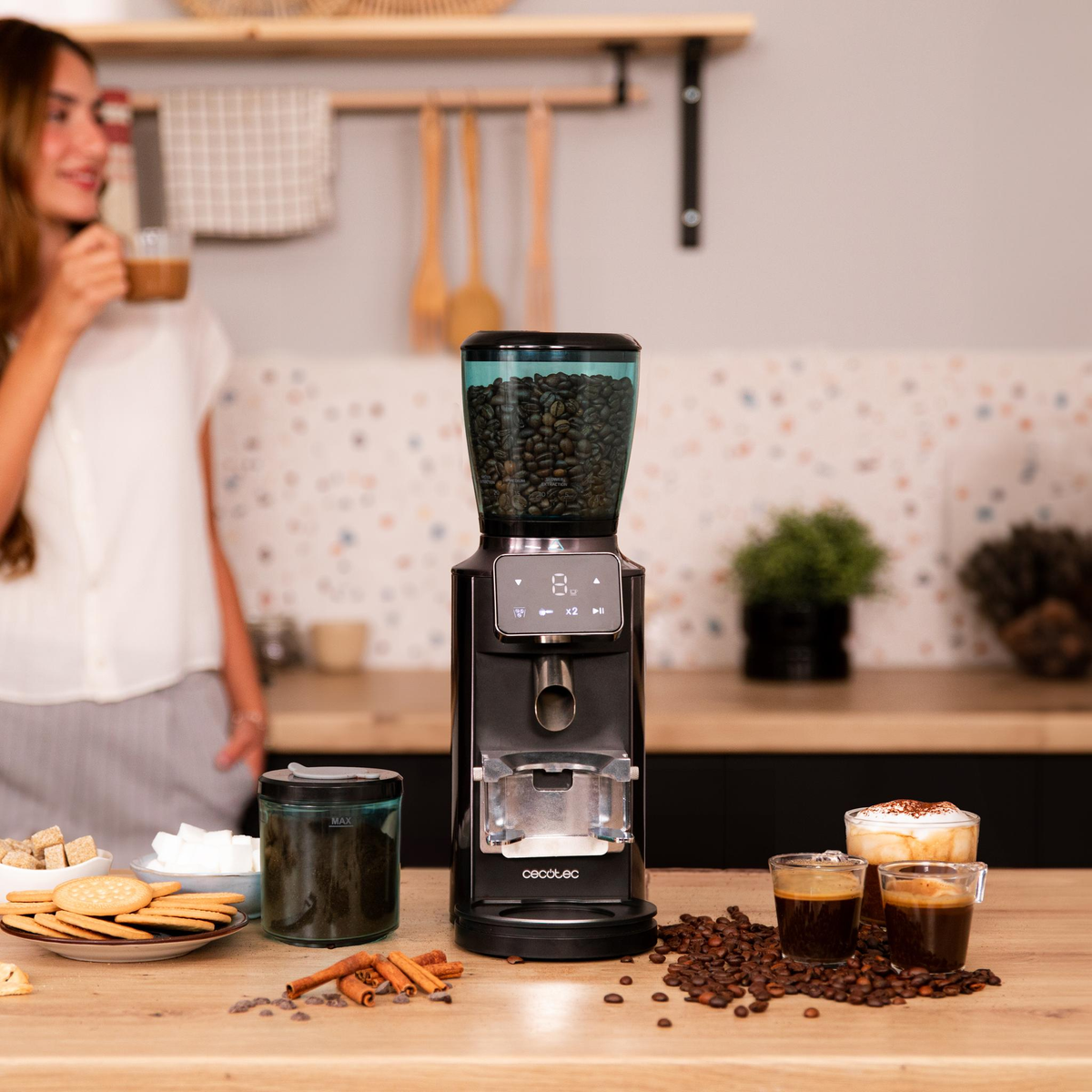 Una donna con macinacaffè, caffè e biscotti su un tavolo di legno.