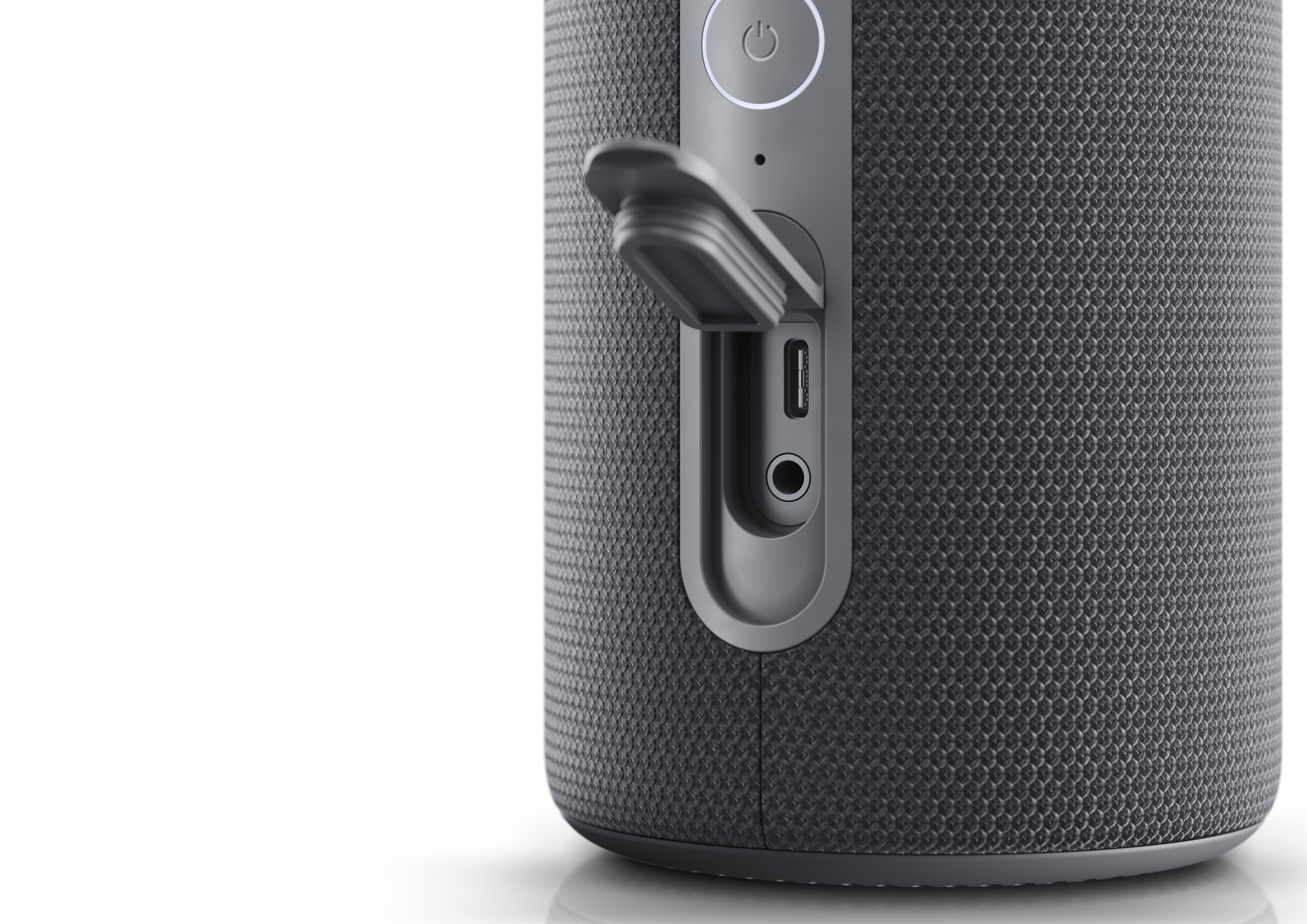 Nahaufnahme eines dunkelgrauen Lautsprechers mit geöffneter Klappe, die USB- und Audioanschlüsse freilegt, vor weißem Hintergrund.
