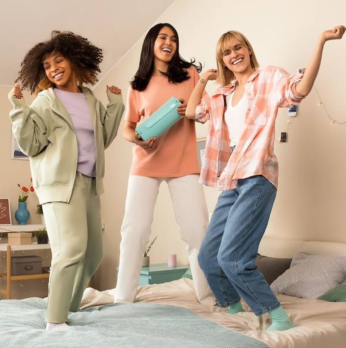Drei Frauen tanzen in einem Raum. Eine hält einen Lautsprecher. Fröhliche Atmosphäre.