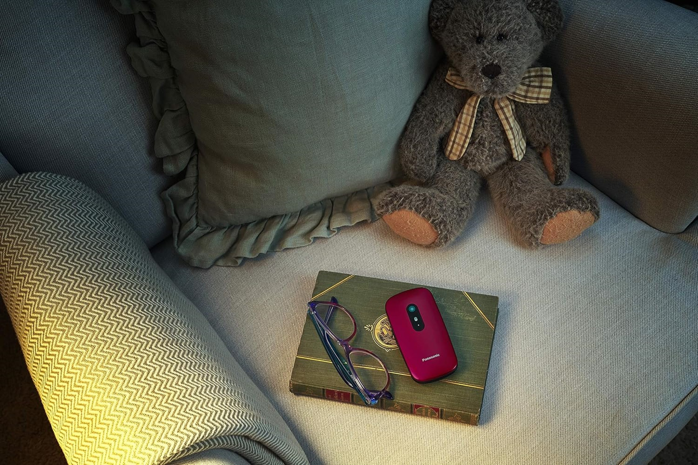 Una escena con un oso de peluche, libro, gafas y un teléfono cerrado en un sillón.