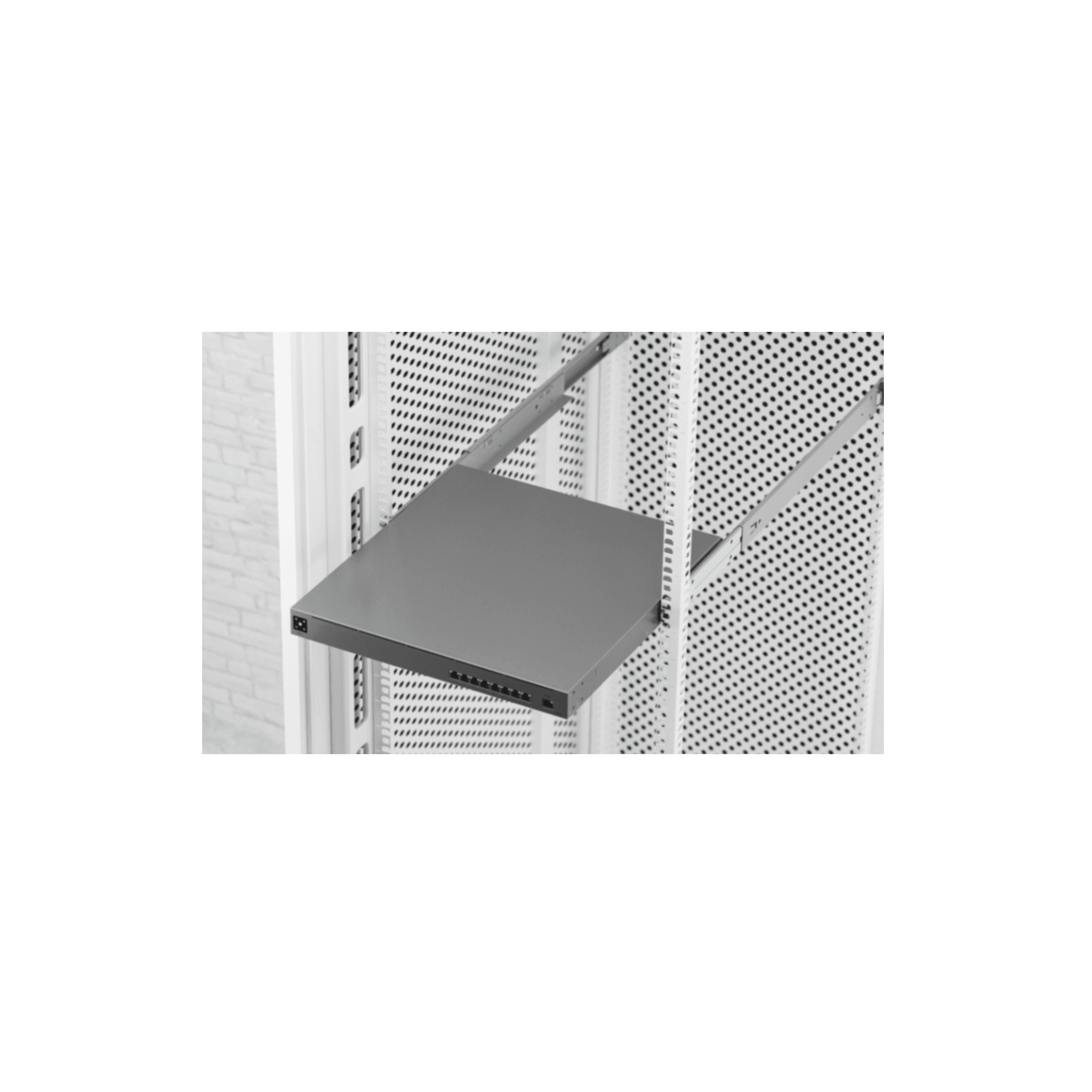 Un estante gris instalado en un bastidor metálico blanco perforado, con pared de ladrillo blanco detrás.