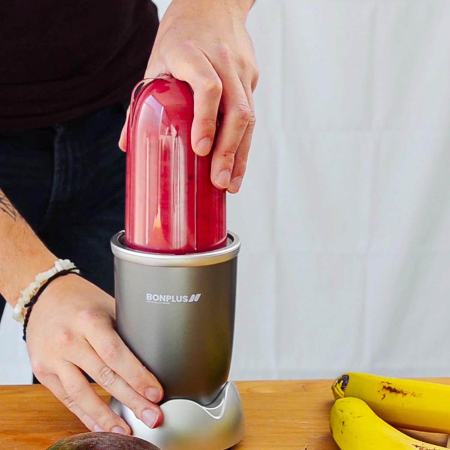 Manos de una persona preparando un batido en una licuadora. Frutas en la mesa.
