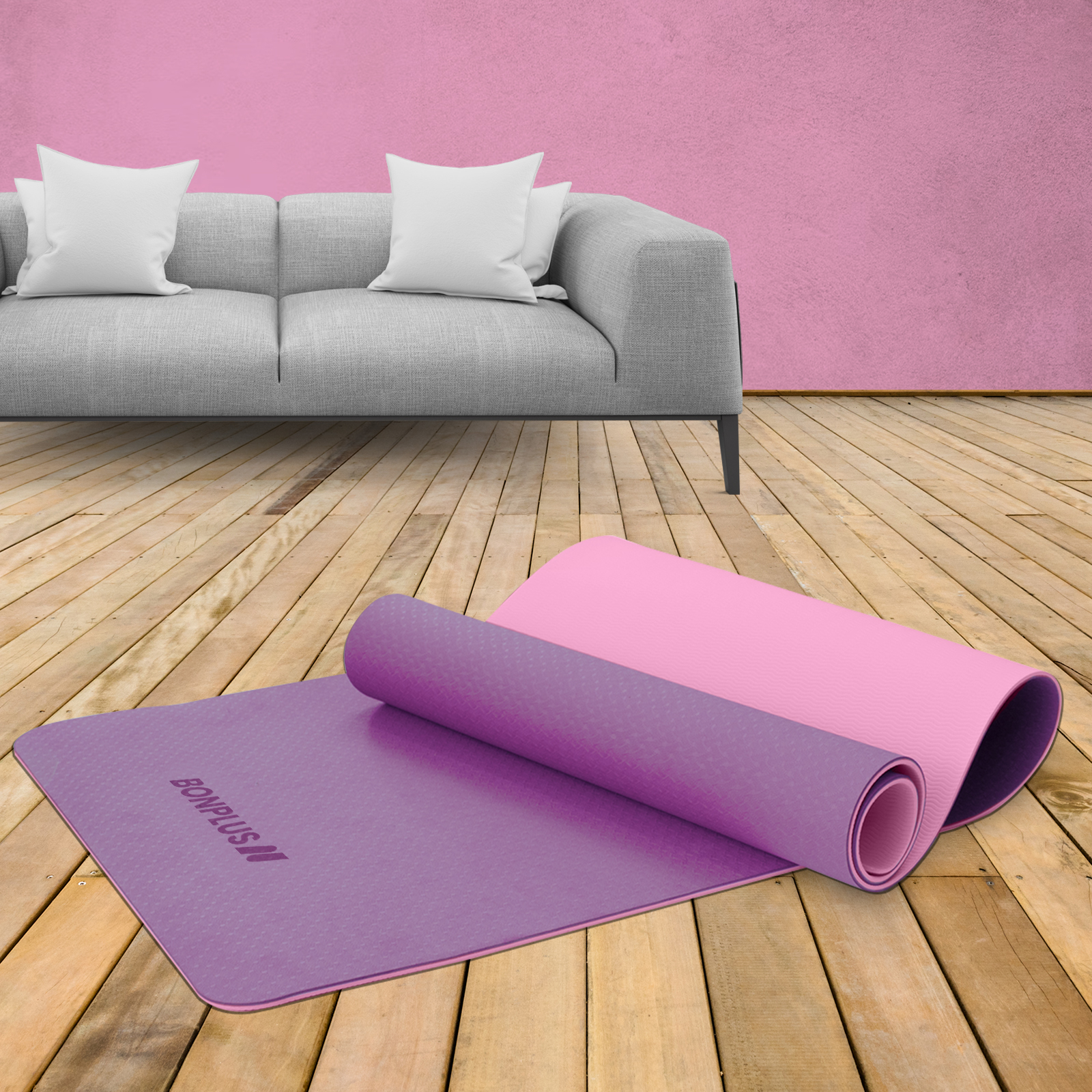 Esterillas de yoga en un suelo de madera con un sofá gris y una pared rosa en el fondo.