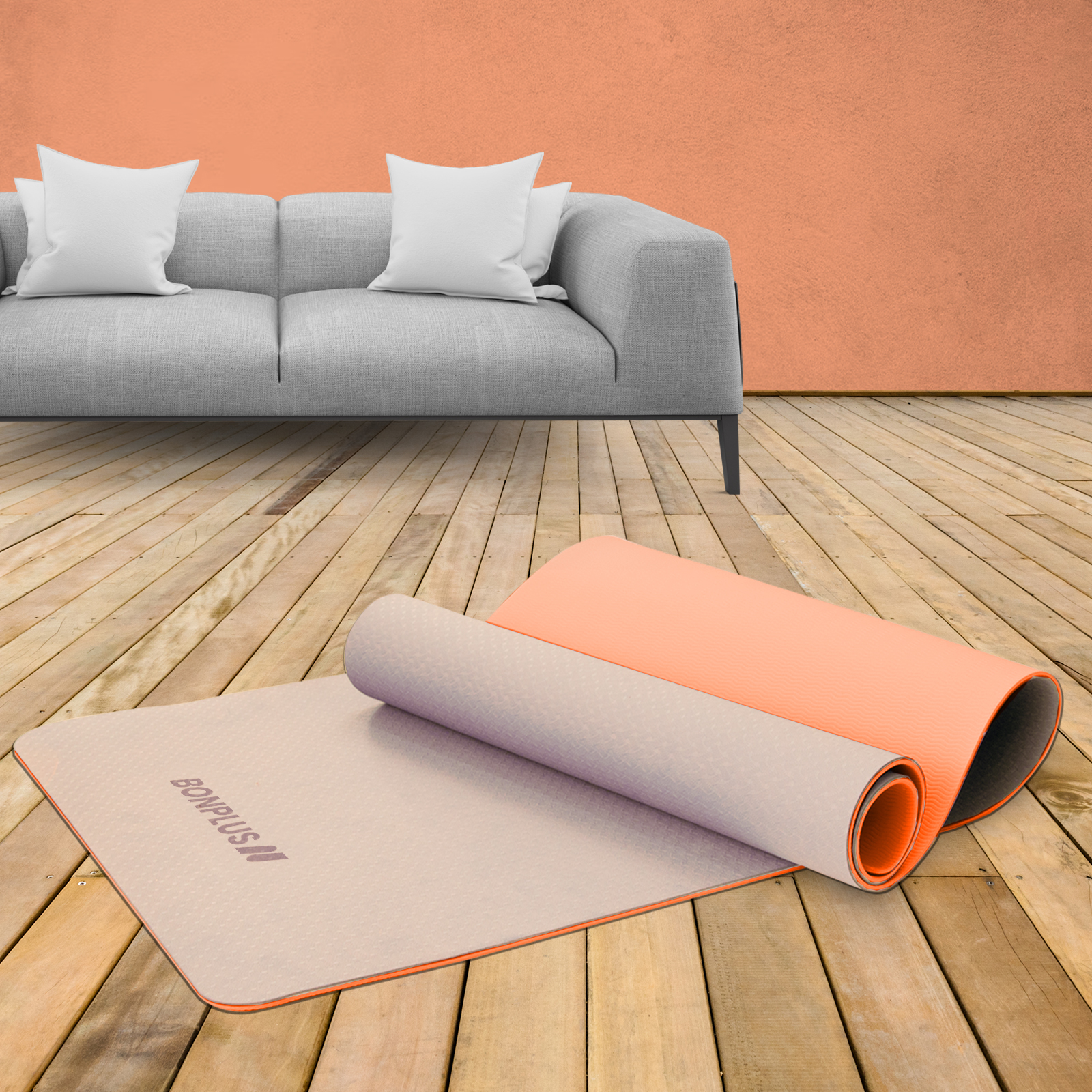 Una esterilla de yoga beige enrollada está en un suelo de madera junto a una extendida. Sofá gris al fondo.