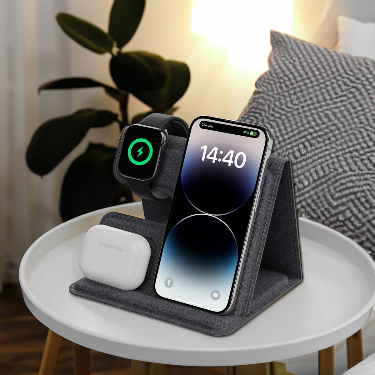 Oplaadstation met een telefoon, horloge en oordopjes op een witte tafel met een plant.