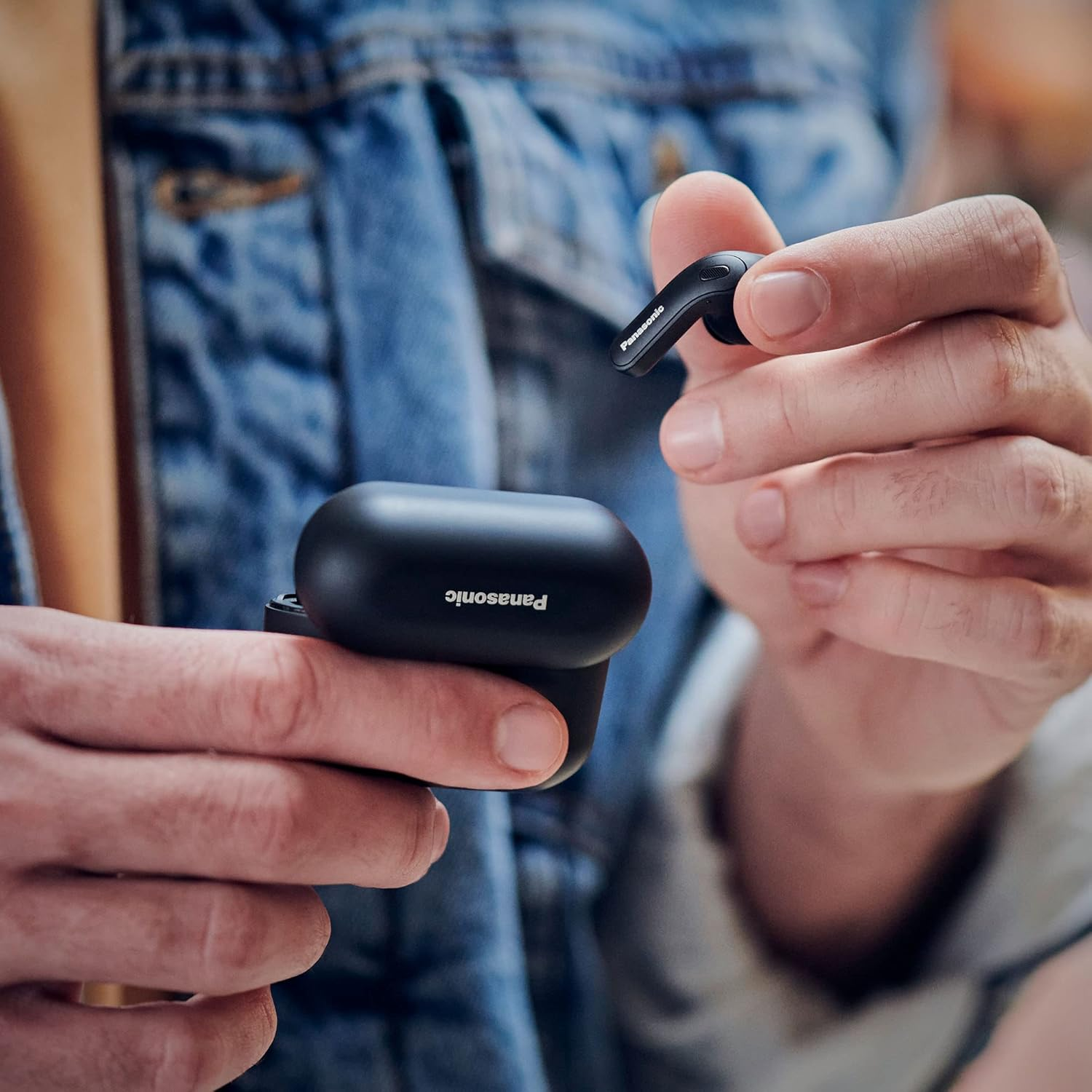 Person hält schwarze Panasonic-Ohrhörer, einen in der Hand, einen im Etui.