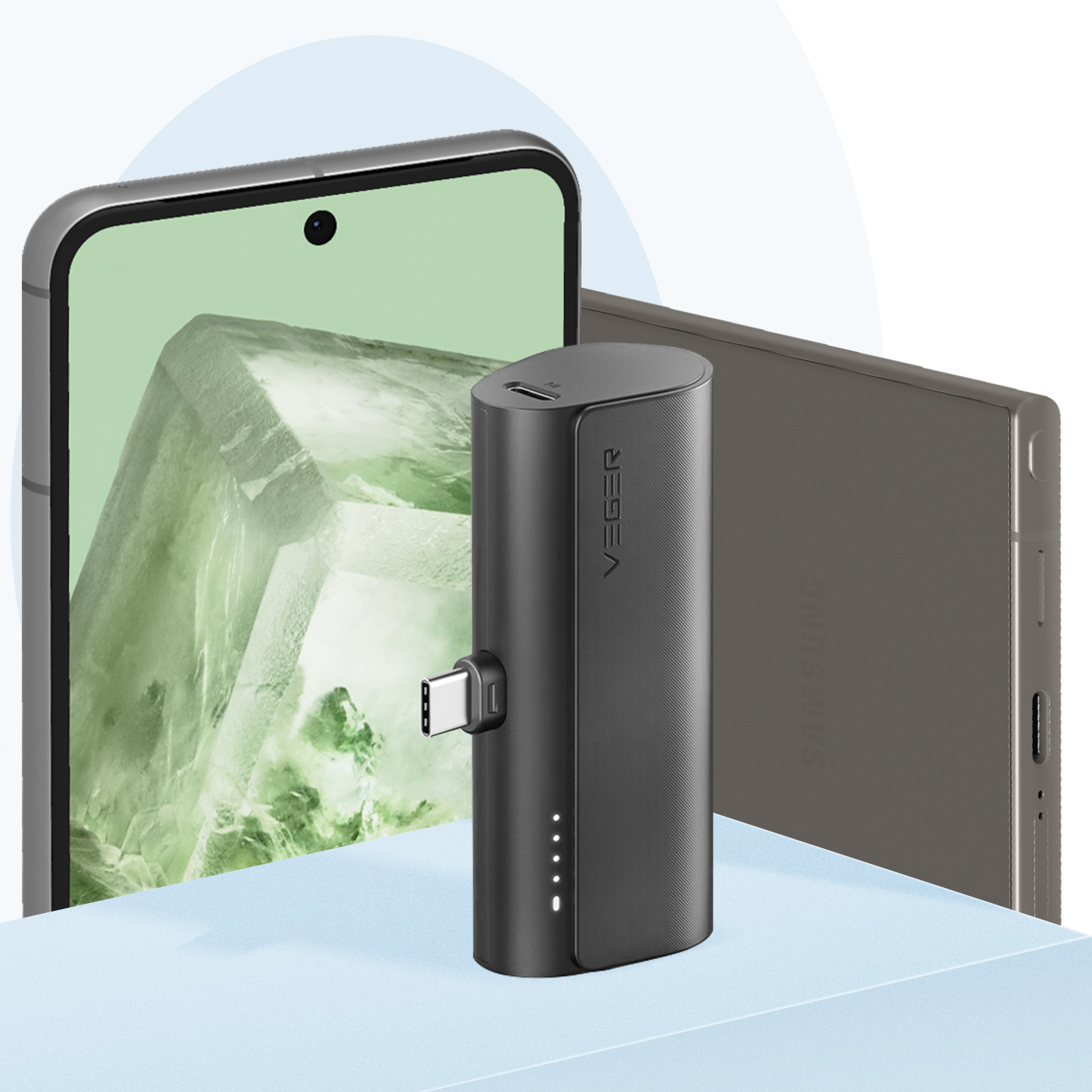 Un power bank nero con porta USB-C accanto a un telefono e un tablet su una superficie blu.