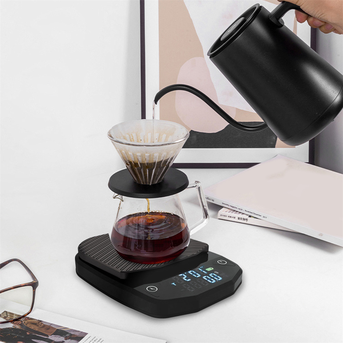 Ein Kaffee-Setup mit Waage, Wasserkocher, Kaffeetropfer und einer Glaskaraffe mit Kaffee. Eine Hand gießt Wasser ein.