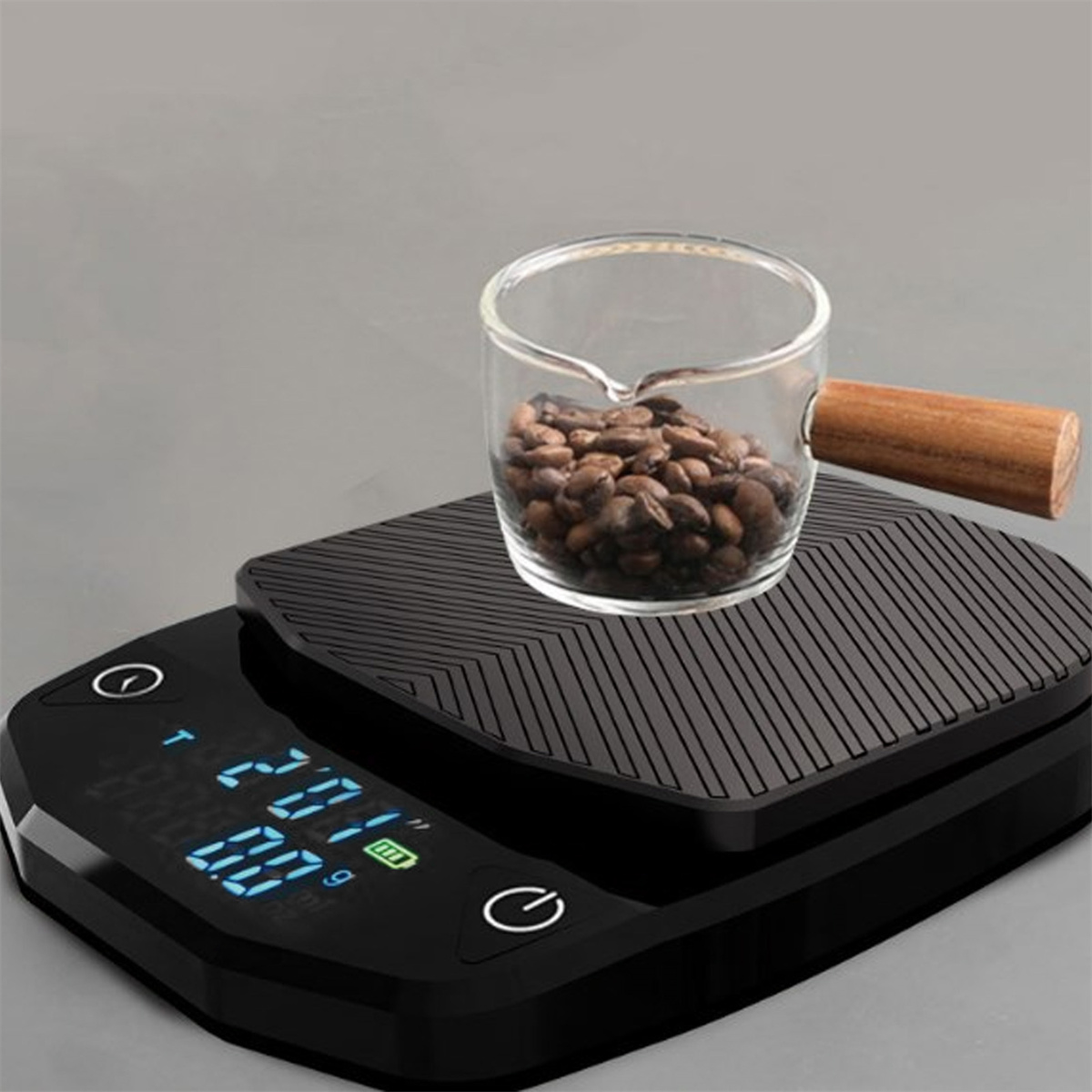 Kaffeebohnen in einem Glasbecher mit Holzgriff auf einer schwarzen Digitalwaage. Grauer Hintergrund.