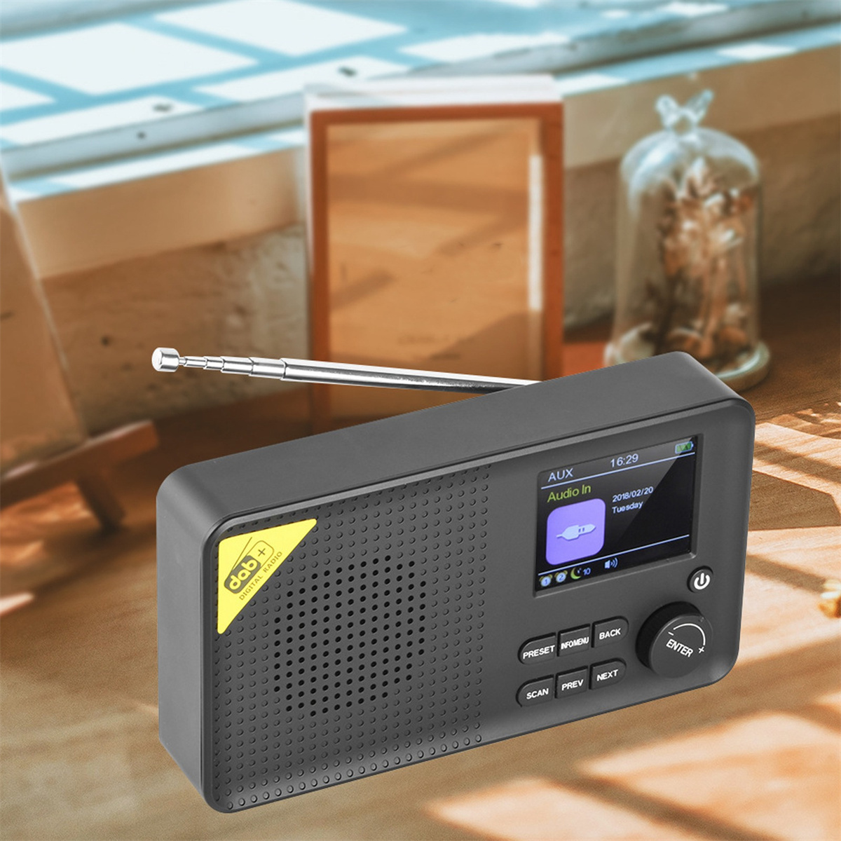 Schwarzes Radio mit kleinem Bildschirm, beschriftet mit DAB+, AUX und Knöpfen. Es steht auf einem Holztisch.