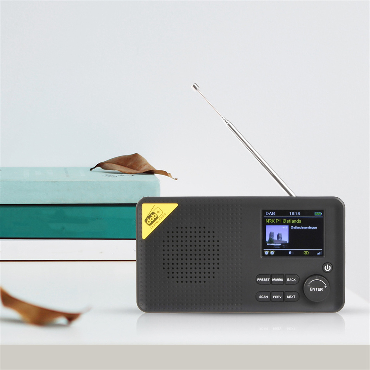 Ein schwarzes DAB-Radio mit kleinem Bildschirm und Metallantenne. Das Radio steht auf weißer Oberfläche.