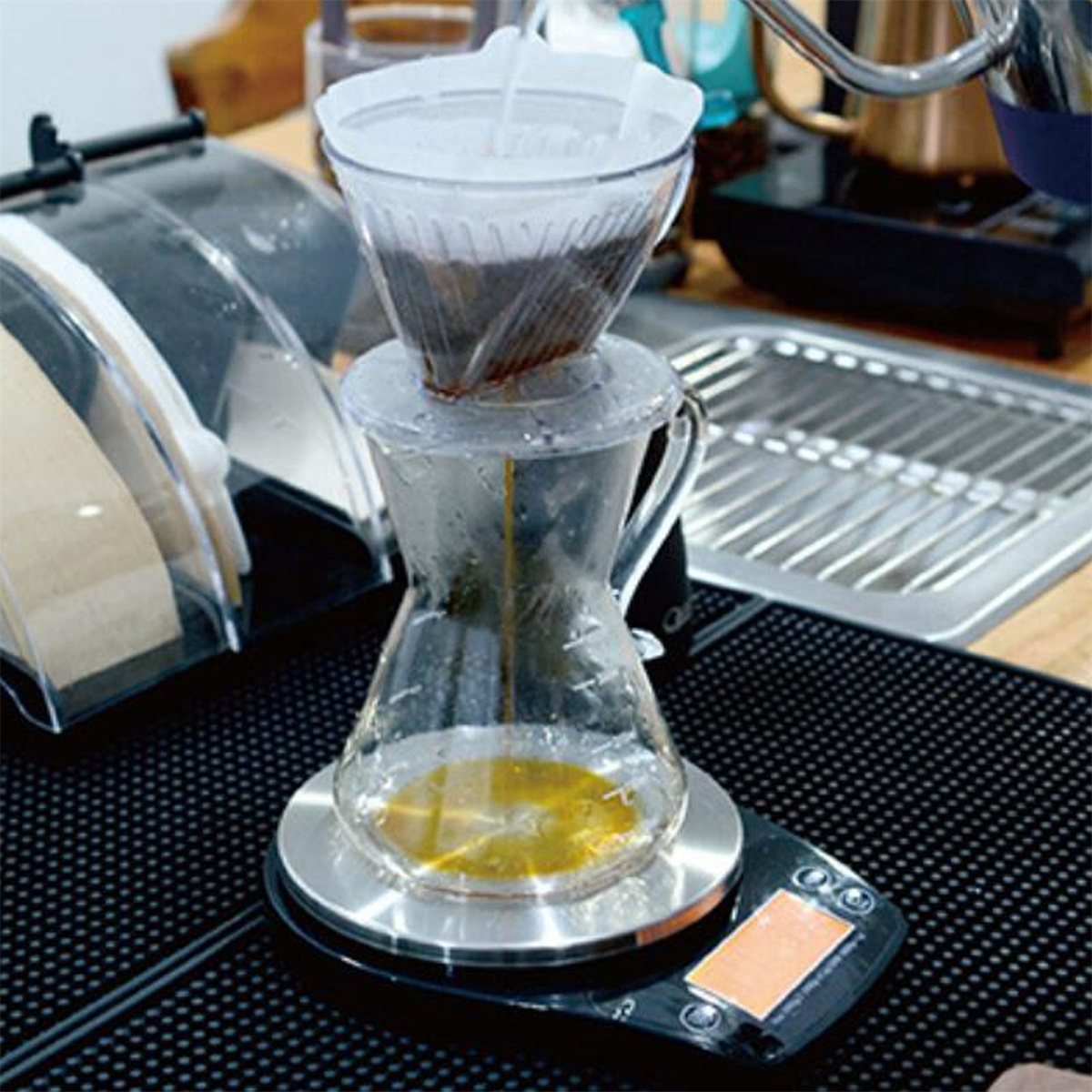 Kaffee wird durch einen Filter gebrüht. Eine Waage befindet sich unter der Glaskaraffe. Der Vorgang wird gezeigt.
