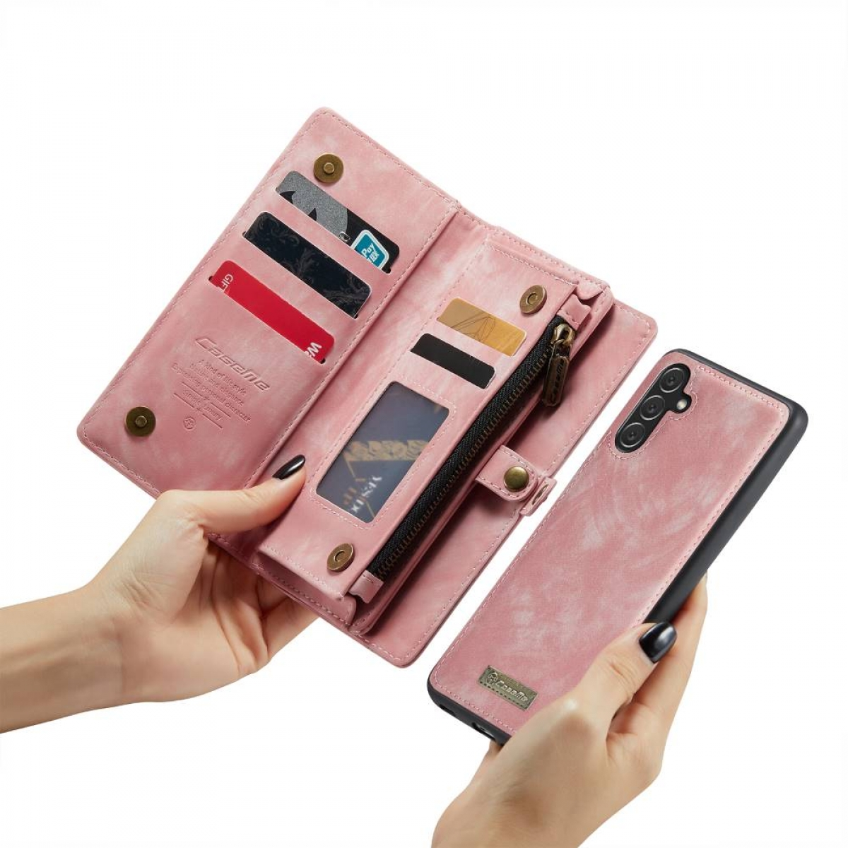 Eine pinkfarbene Brieftaschen-Handyhülle, geöffnet, mit Karten und einem Telefon. Je eine Hand hält.