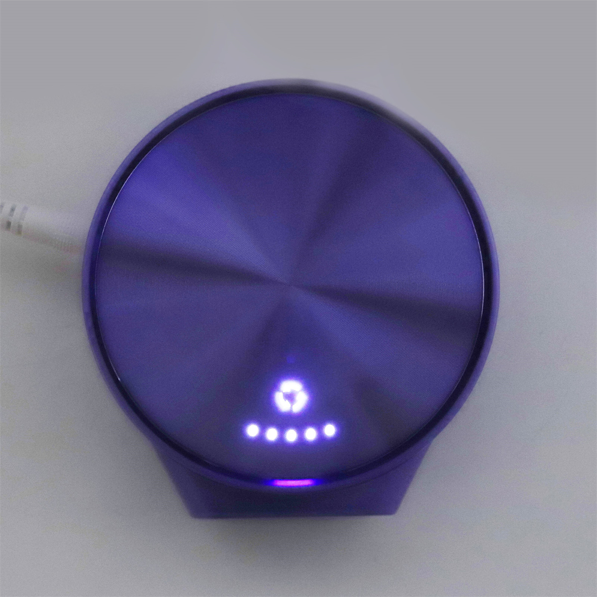Ein lila kreisförmiges Gerät mit leuchtendem Ring. Es hat ein weißes Kabel und Lichter.