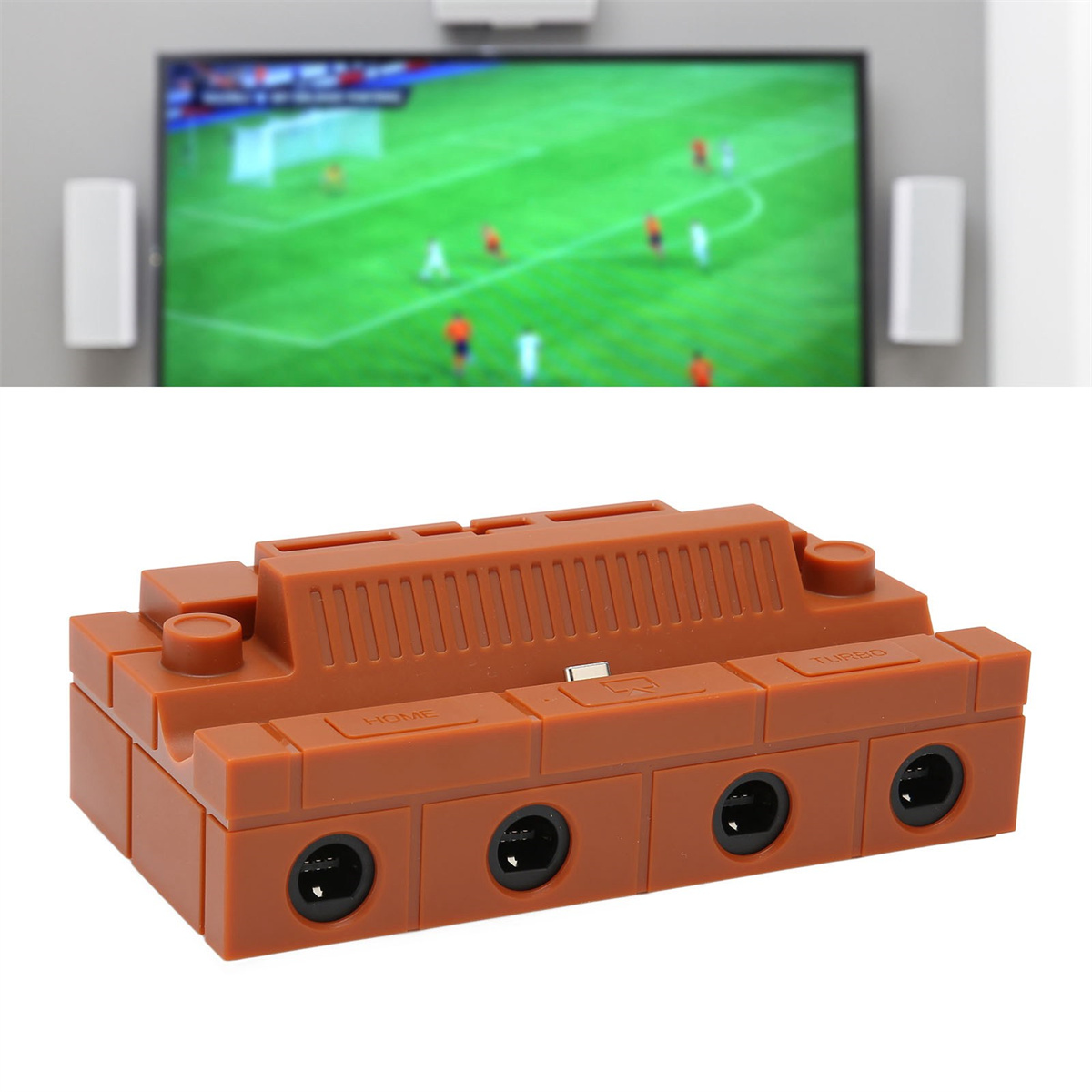 Eine braune Spielkonsole mit mehreren Anschlüssen, vor einem TV-Gerät mit Fußballspiel.