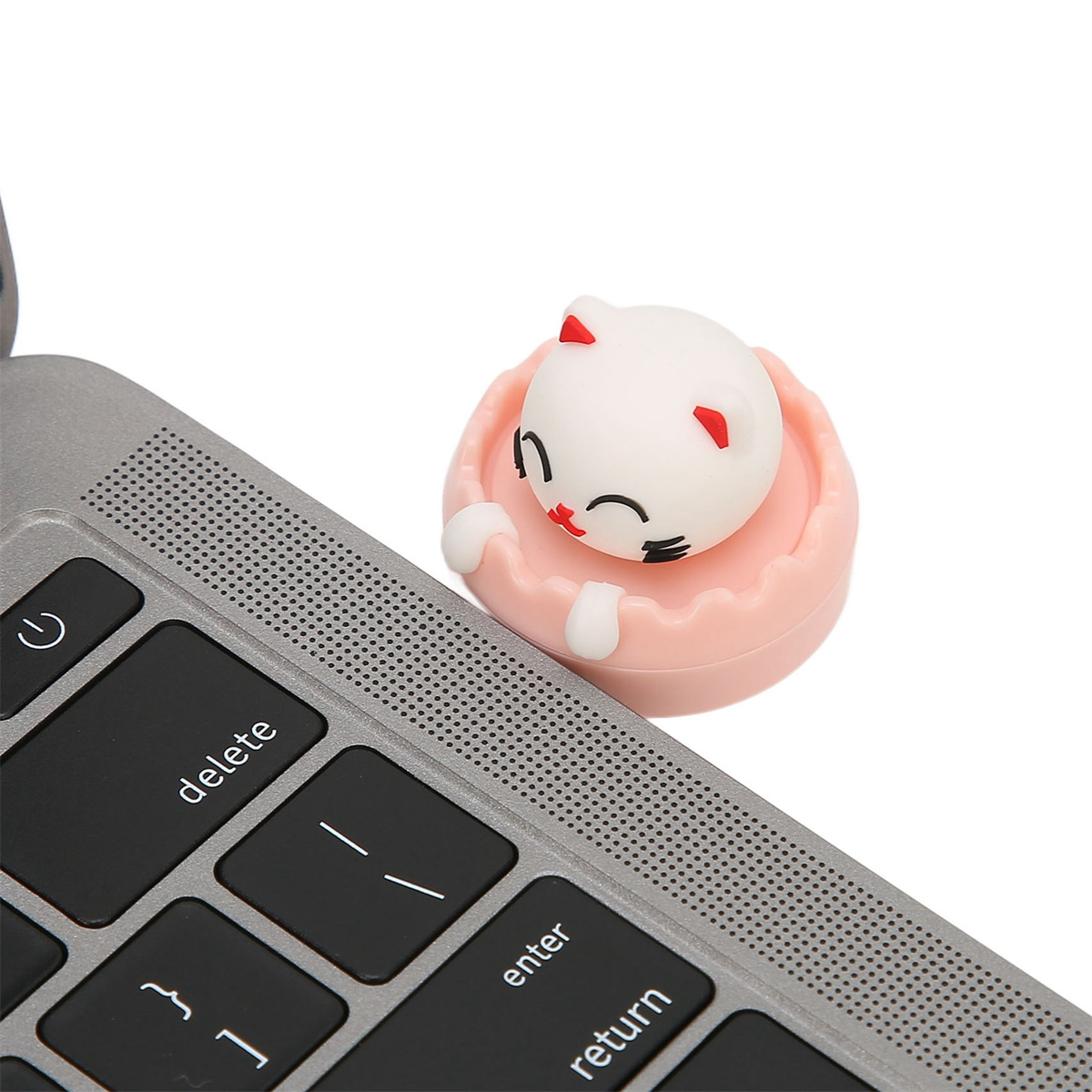 Eine Spielzeugkatze auf einer Laptop-Tastatur. Die Katze ist weiß mit rosa Details, in einer rosa Schale.