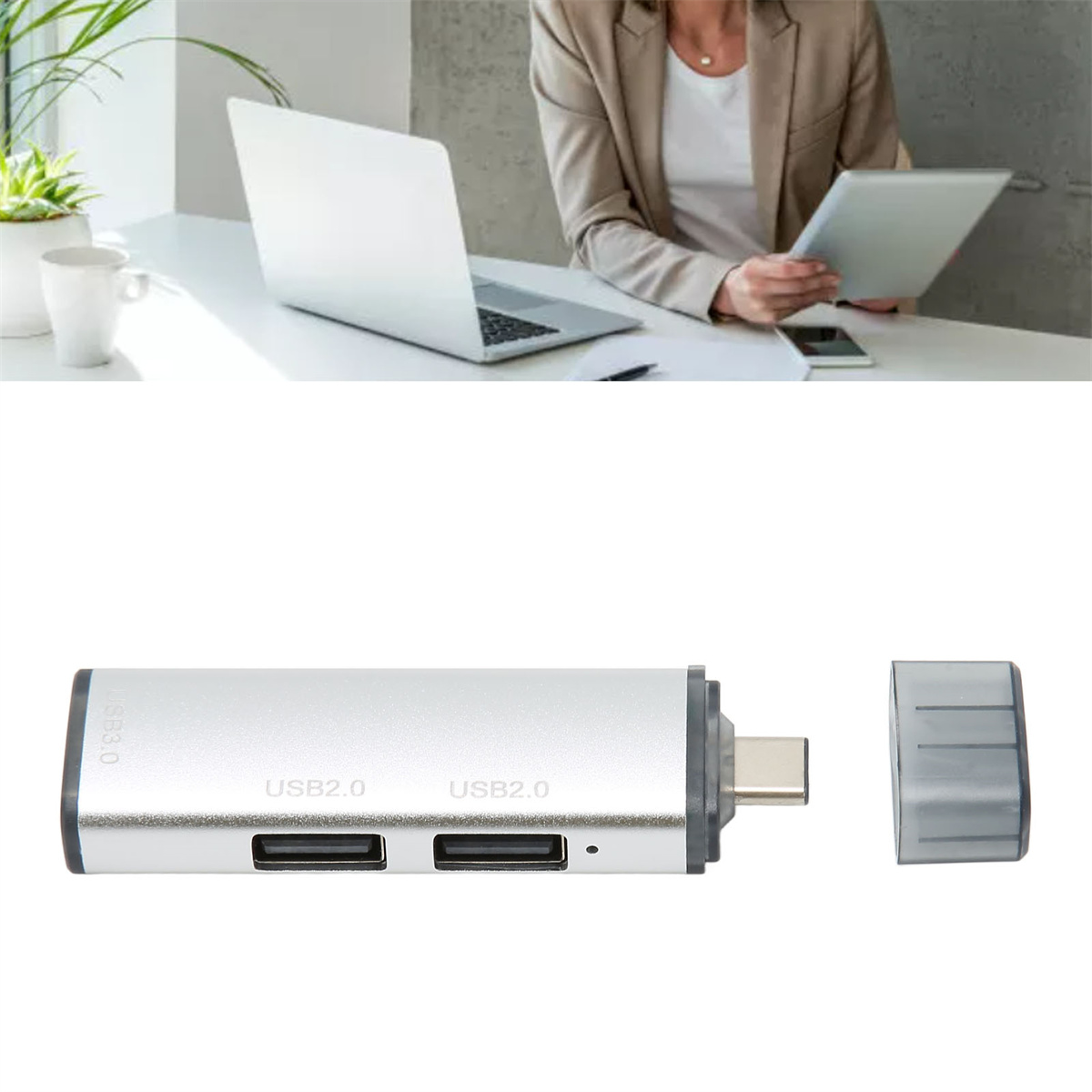 Eine Frau arbeitet mit Laptop und Tablet. Ein silberner USB-Hub ist im Vordergrund.