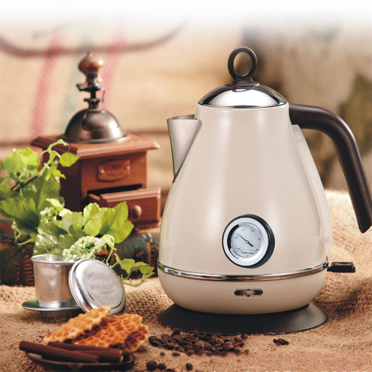 Beige elektrische Kaffeekanne mit schwarzem Griff, Kaffeemühle und Gebäck auf dem Tisch.