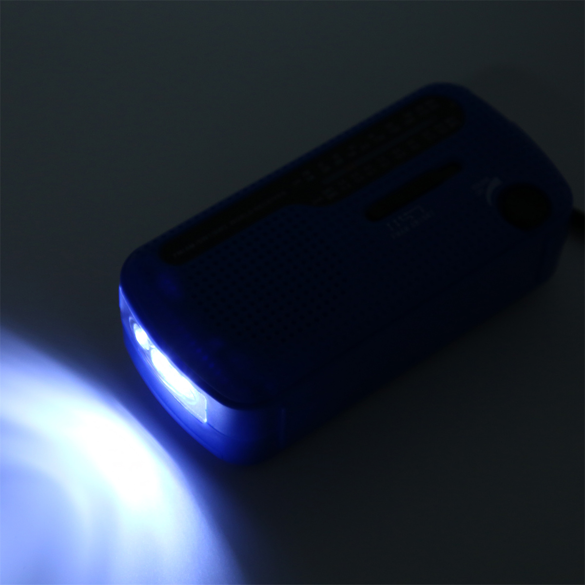 Blaues Notfallradio mit Taschenlampe, das hellweißes Licht aussendet, vor grauem Hintergrund.