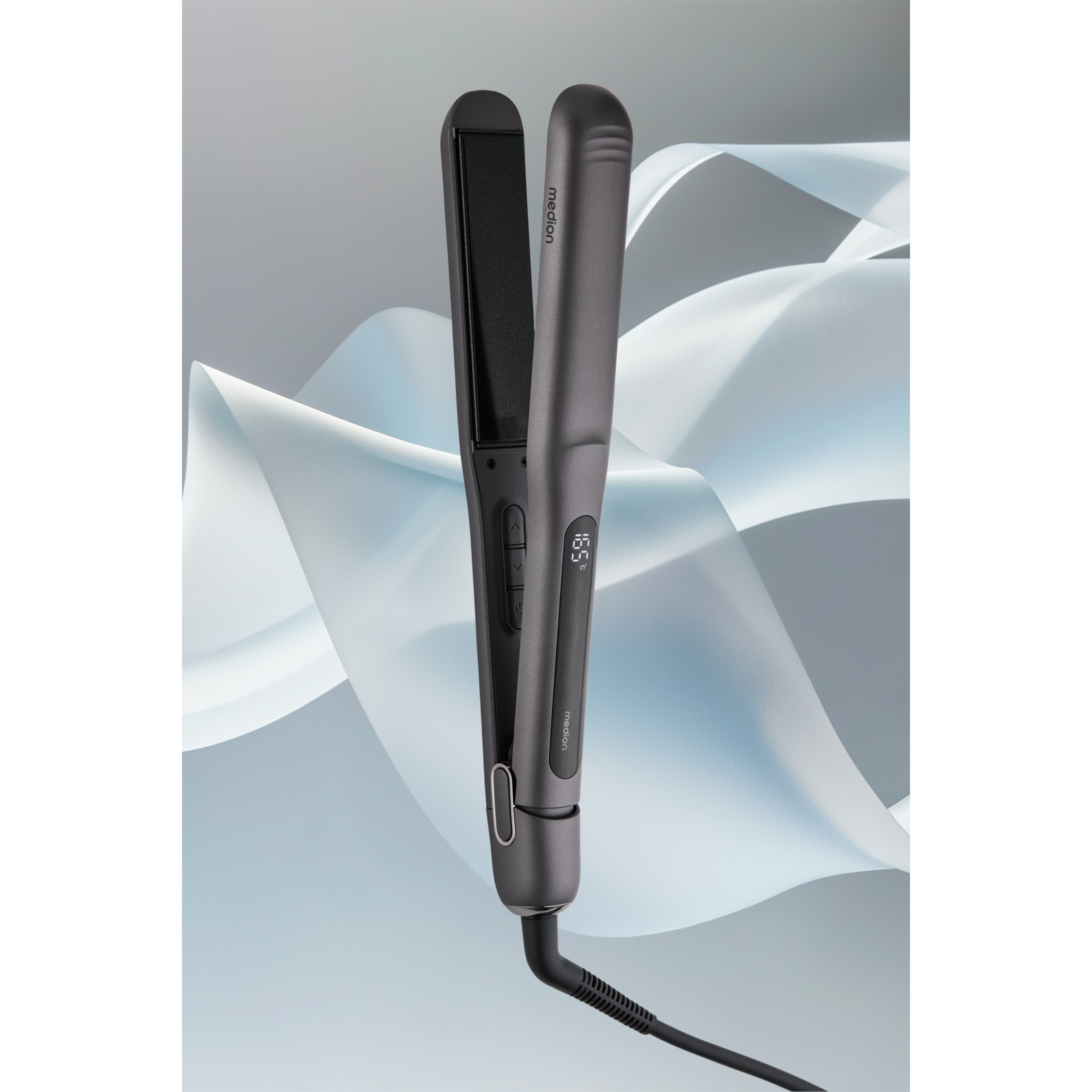 Szara prostownica do włosów z cyfrowym wyświetlaczem. Ma czarny przewód i jest na falistym tle.