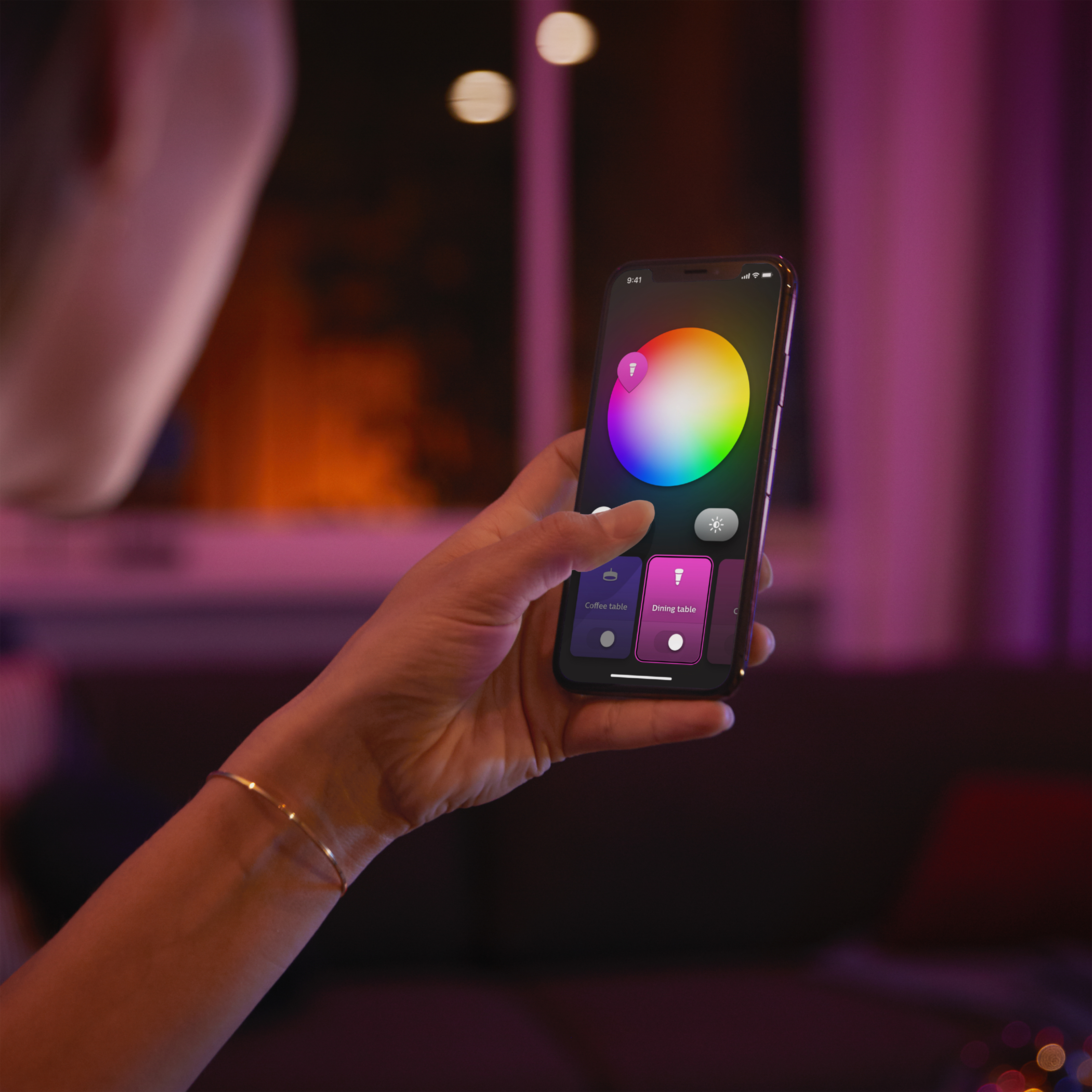 Ręka trzymająca telefon z interfejsem koła kolorów do sterowania oświetleniem.