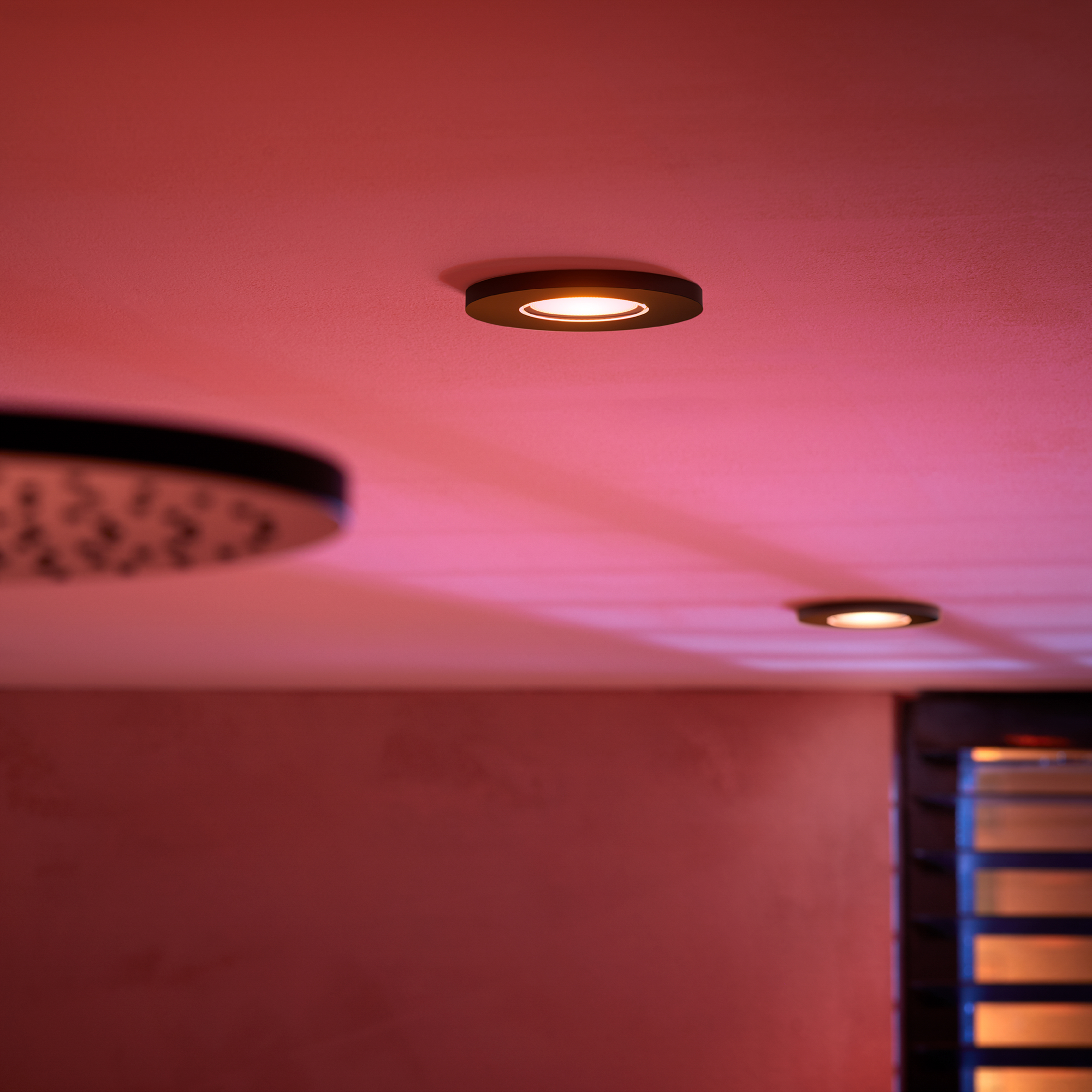 Twee plafondlampen in een roze verlichte kamer, één met een lichtring.