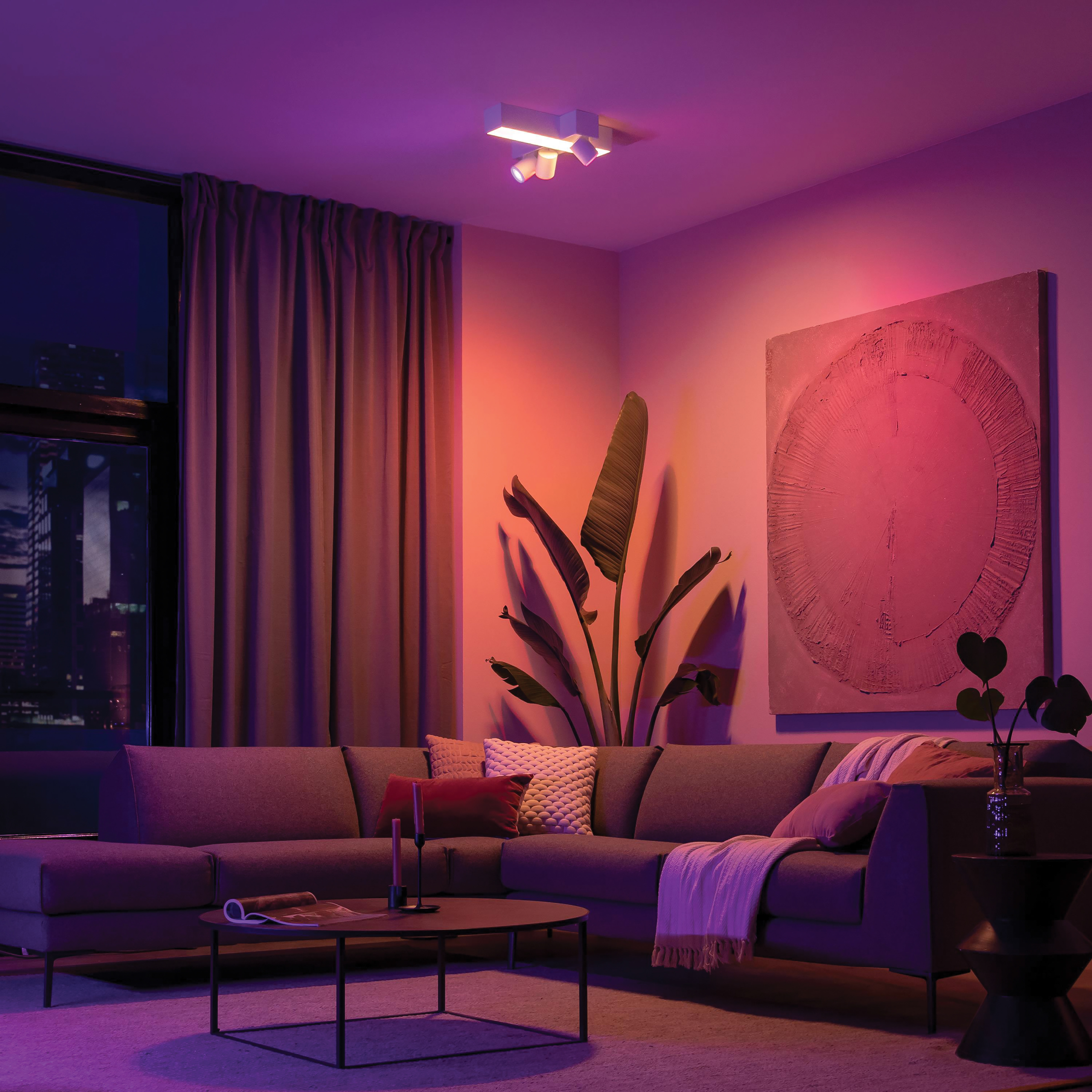 Een woonkamer met een moderne bank, plant en muurkunst, verlicht door een spot.