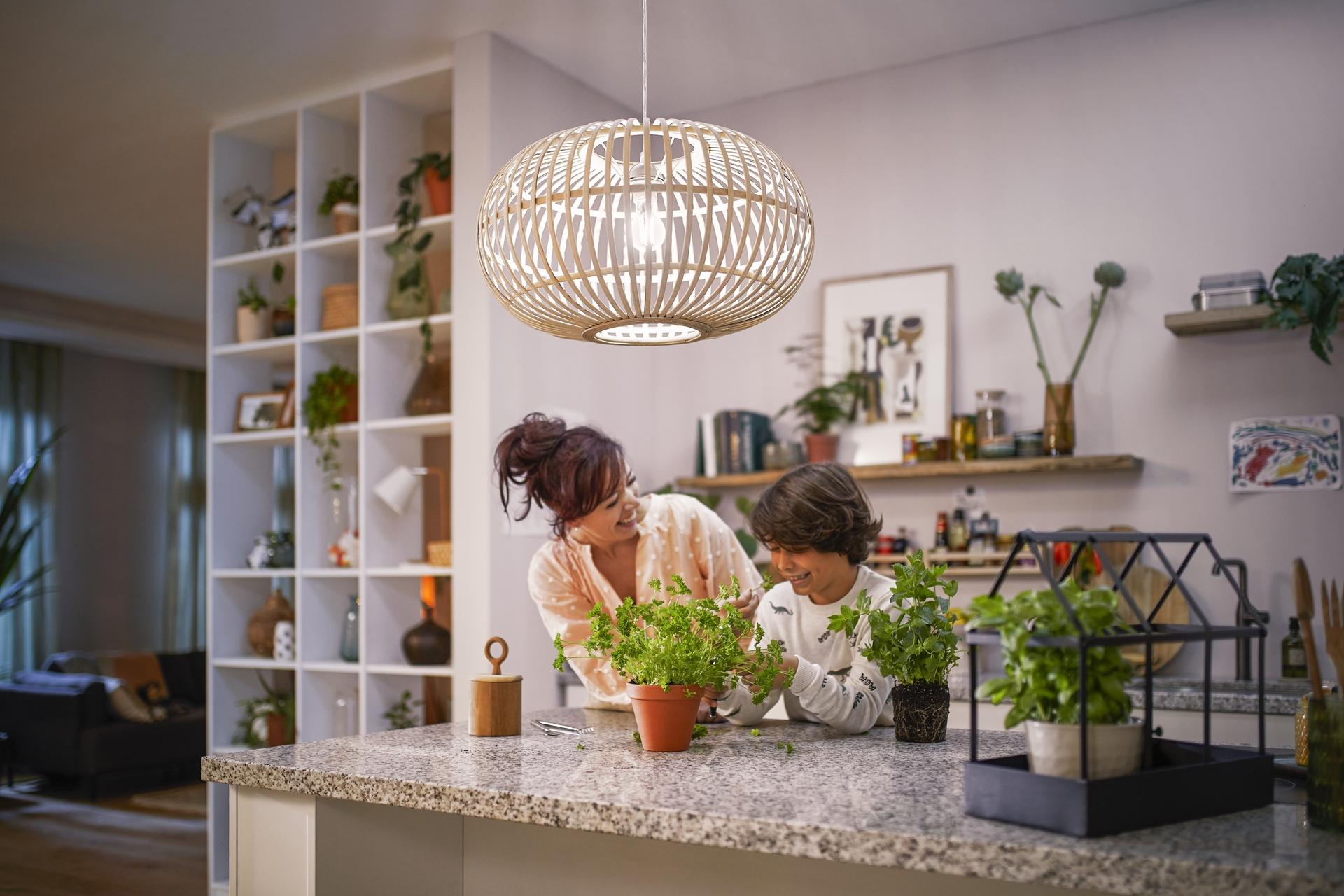 Une mère et son fils dans une cuisine s'occupant de plantes sous un abat-jour en bois ouvert.