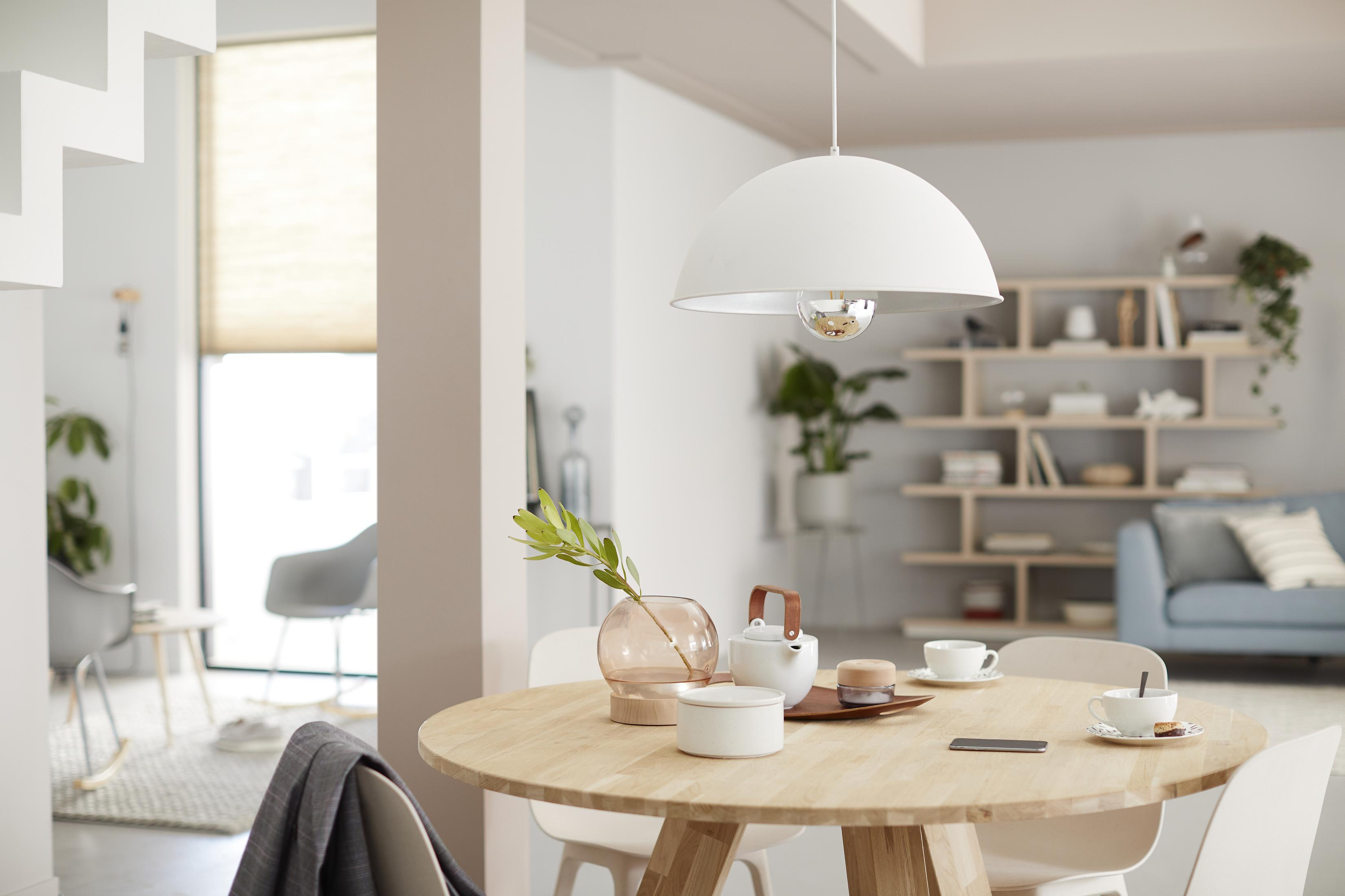 Ein modernes Esszimmer mit einem runden Holztisch, einer weißen Pendelleuchte und einem Sofa.