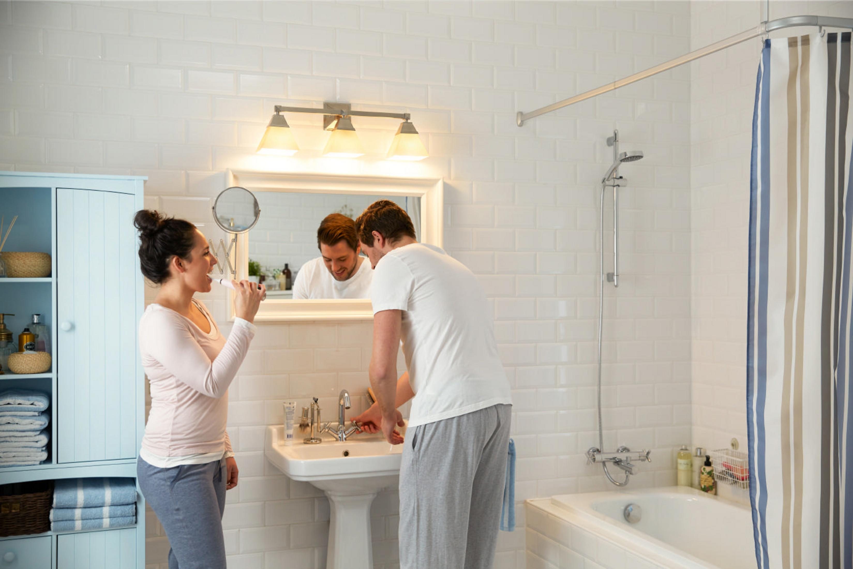 Ein Paar im Badezimmer. Die Frau putzt sich die Zähne, und der Mann wäscht sich die Hände.