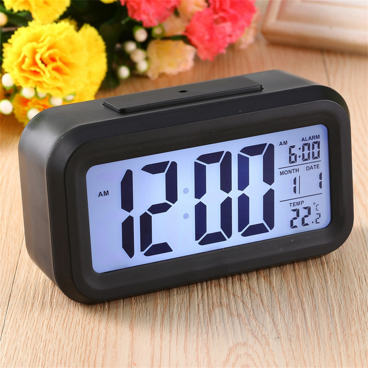 Schwarzer digitaler Wecker mit Anzeige 12:00 AM, Datum und Temperatur. Alarm für 6:00 Uhr morgens eingestellt.