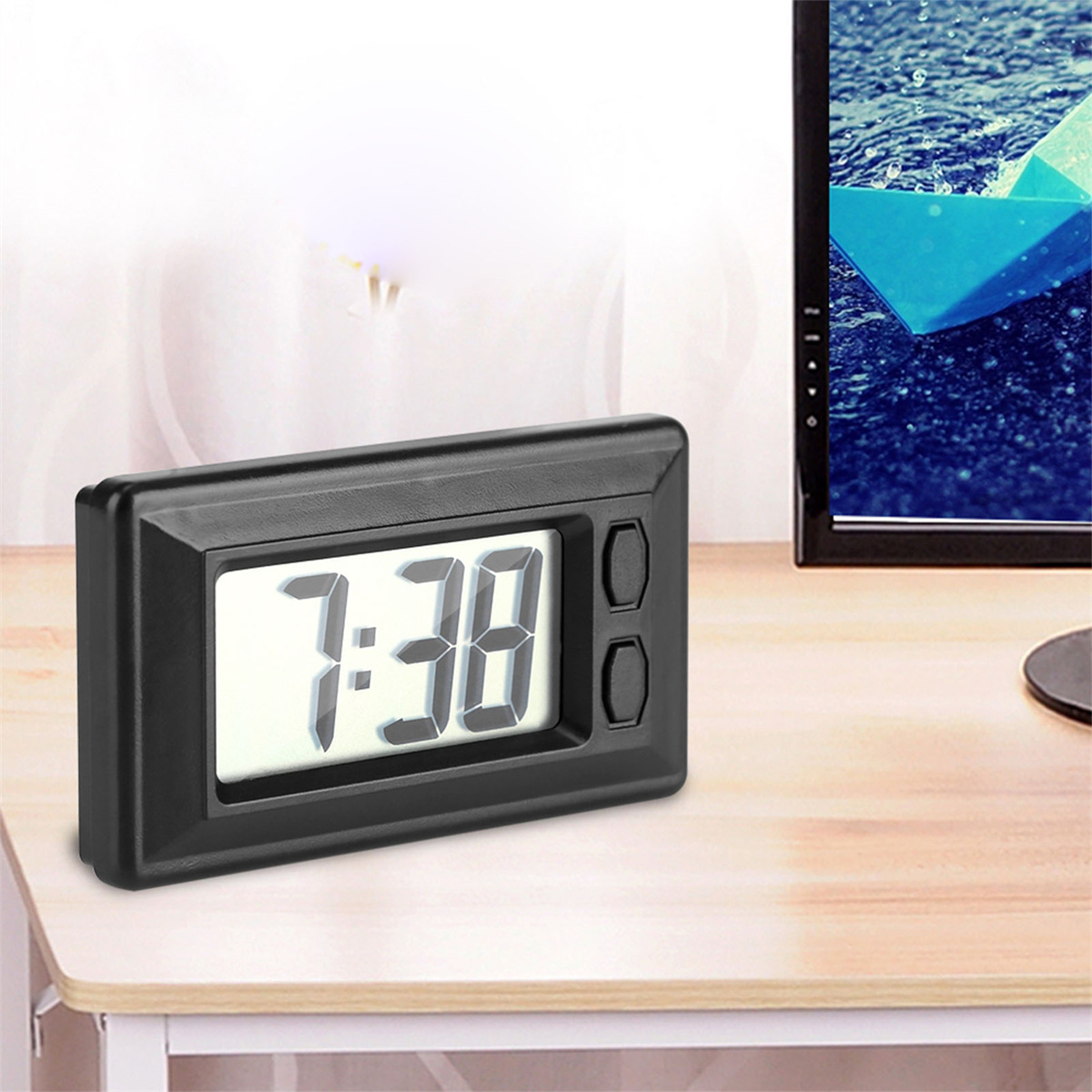 Eine schwarze Digitaluhr mit 7:38, auf einer Holzoberfläche neben einem Monitor.