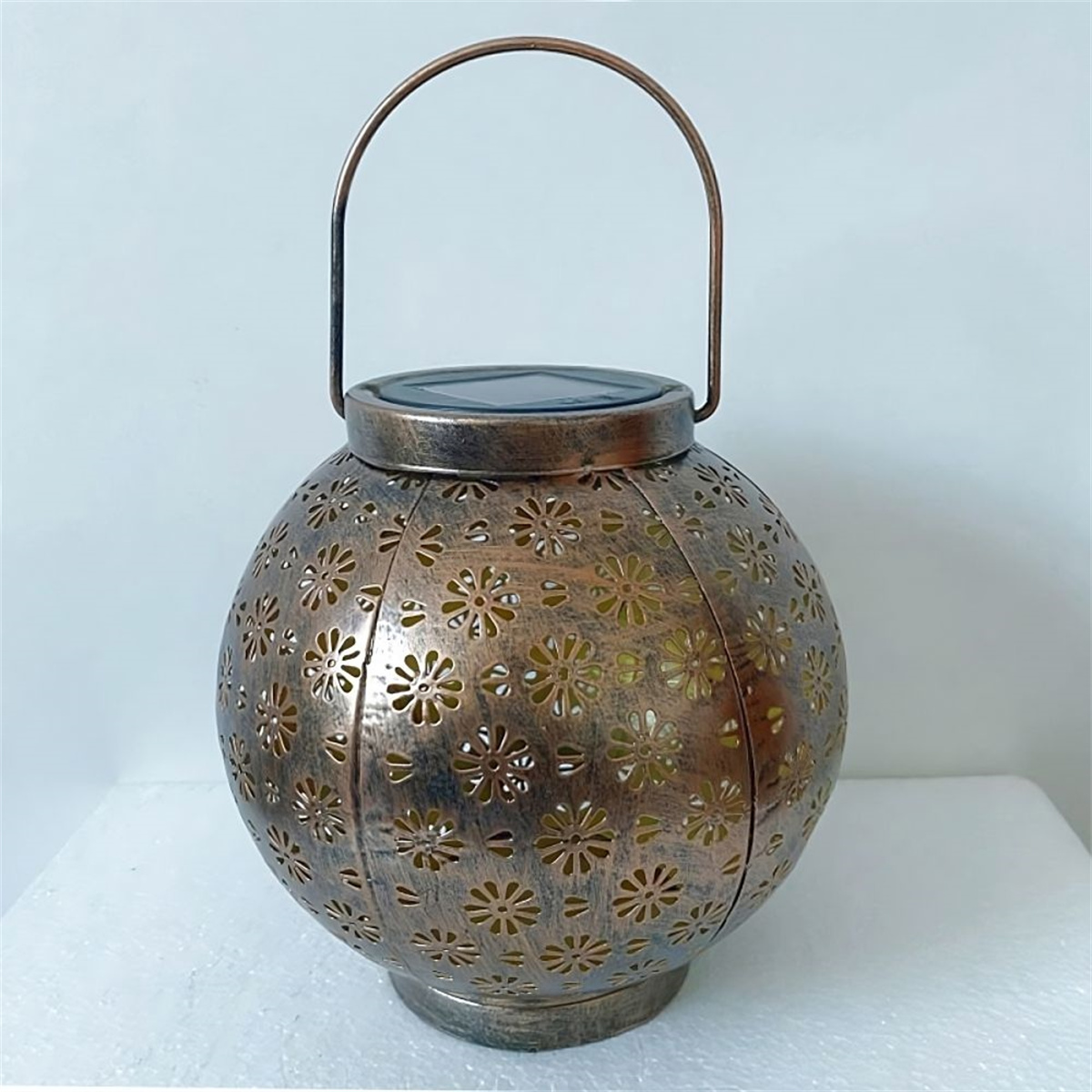 Eine dekorative Metalllaterne mit floralen Ausschnitten, mit Henkel und runder Form.