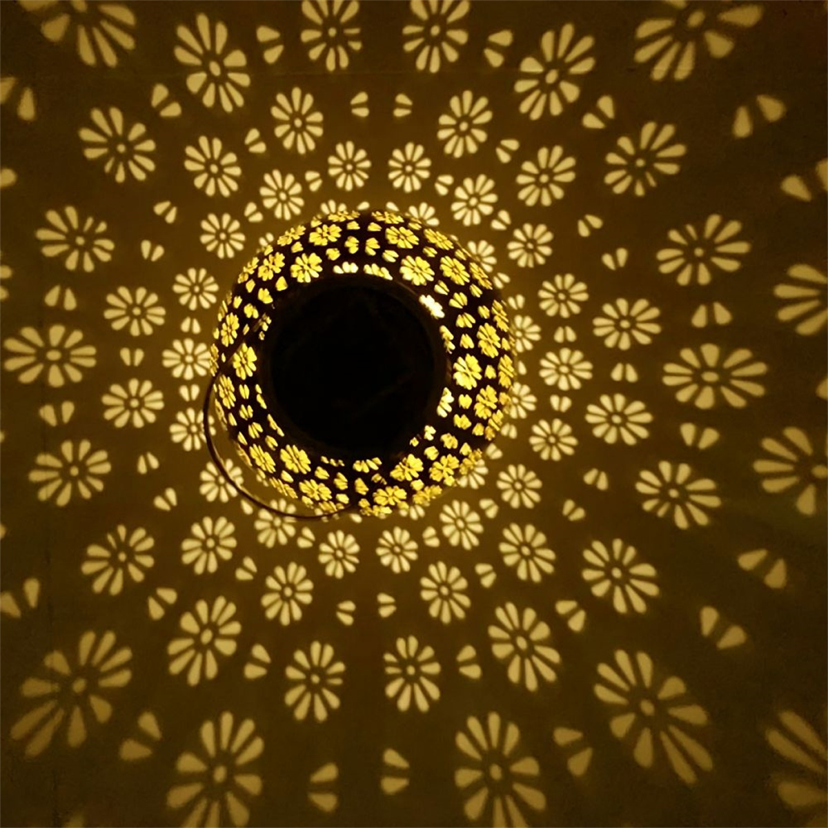Eine Lampe, die ein Blumenmuster auf die darunter liegende Oberfläche wirft. Die Lampe ist goldfarben.