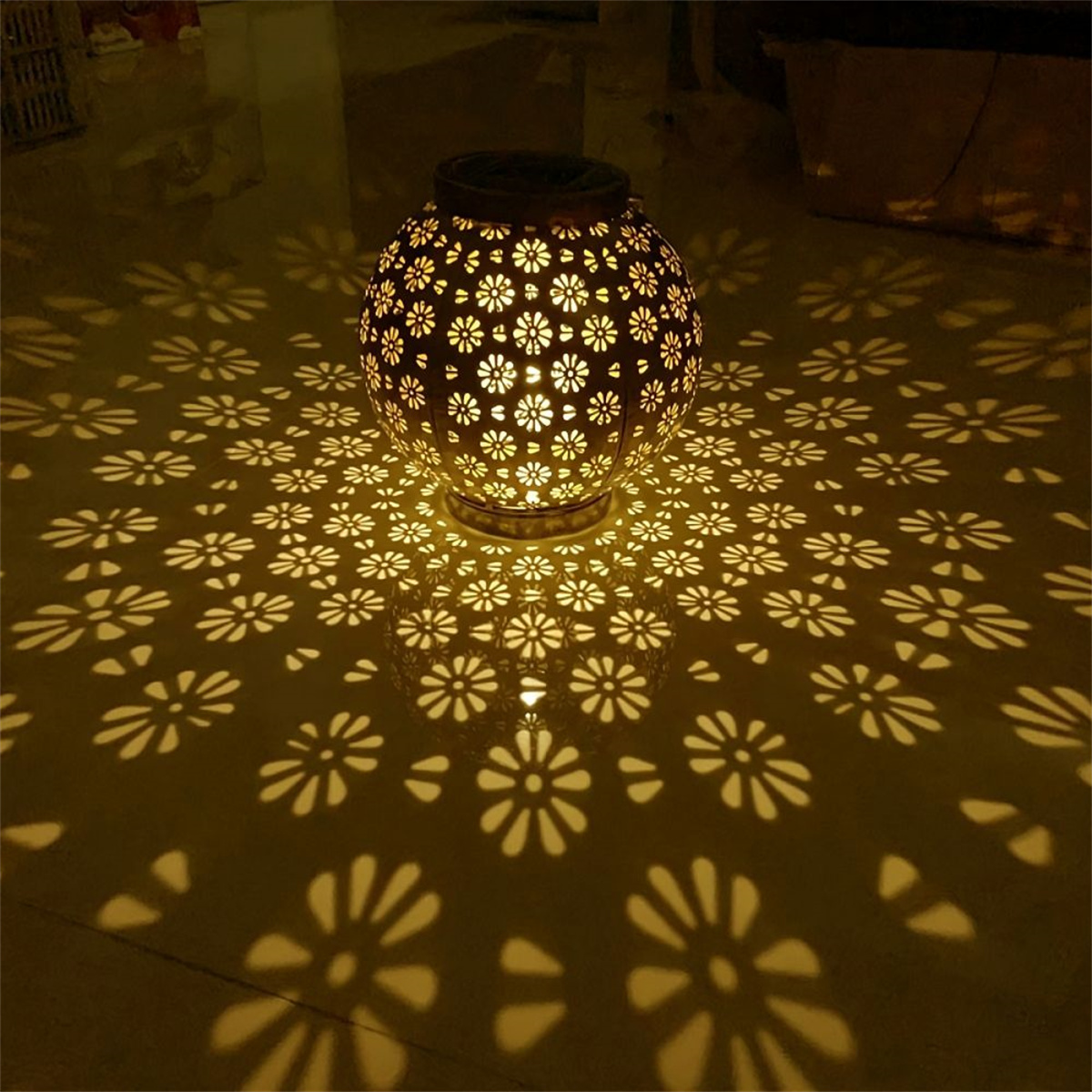Eine Metalllaterne mit ausgeschnittenen Blumen, die Lichtmuster auf eine Oberfläche projizieren. Das Licht ist golden.