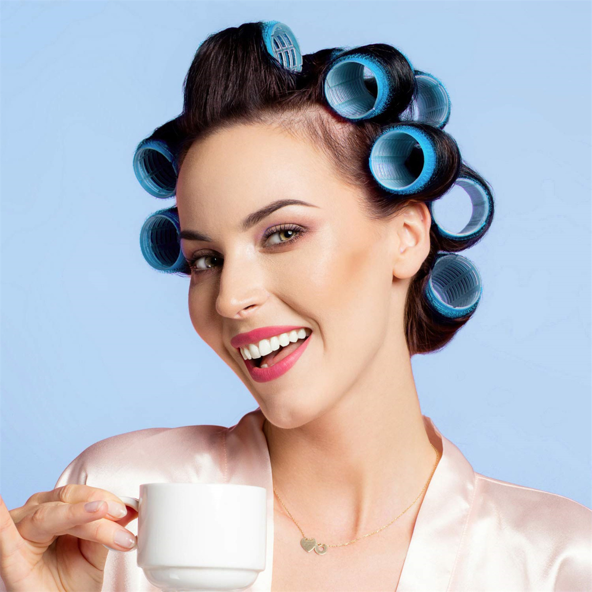 Frau mit Lockenwicklern im Haar, lächelnd, hält eine Tasse und trägt eine Halskette.