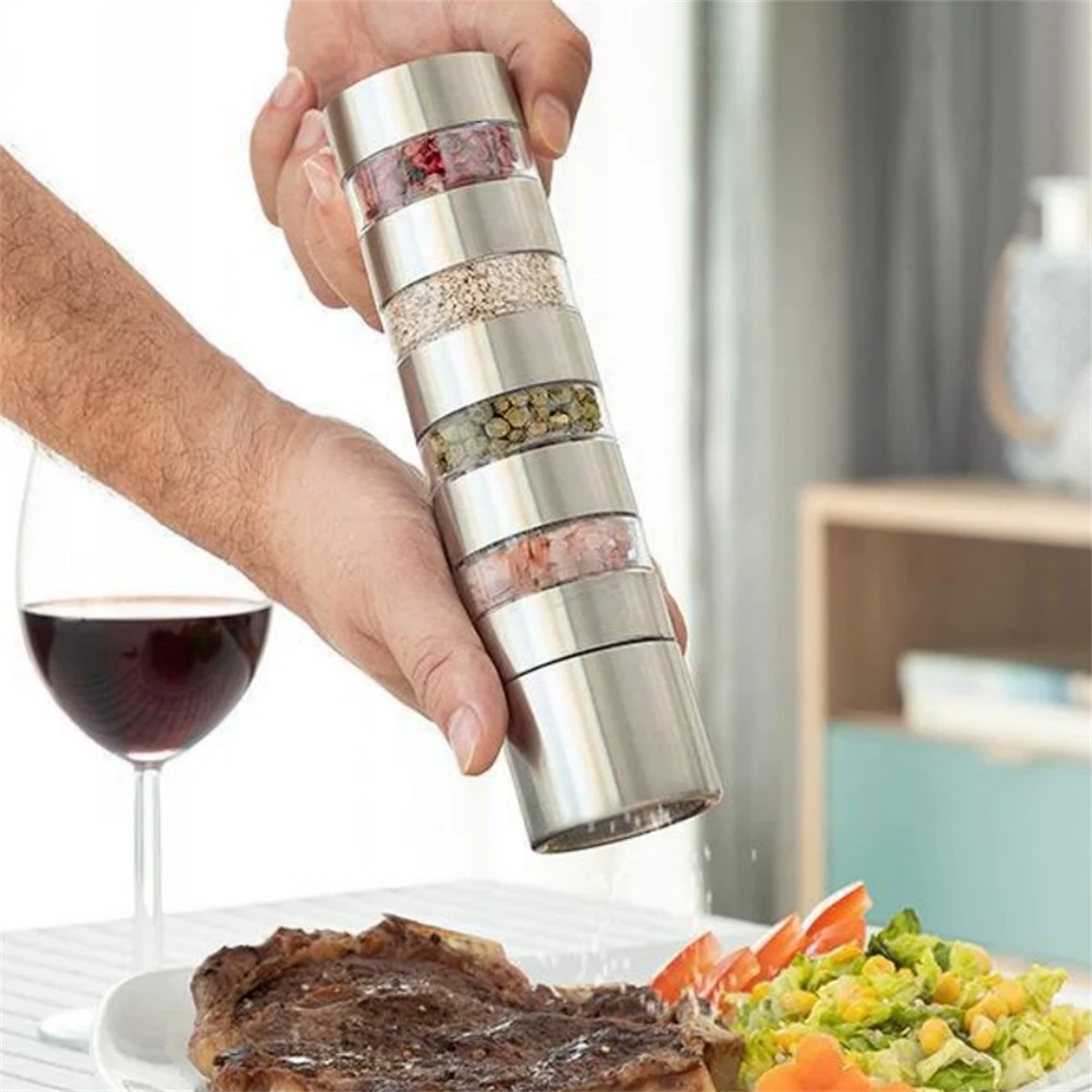 Hand hält einen mehrteiligen Gewürzstreuer über Steak und Salat. Ein Glas Wein.