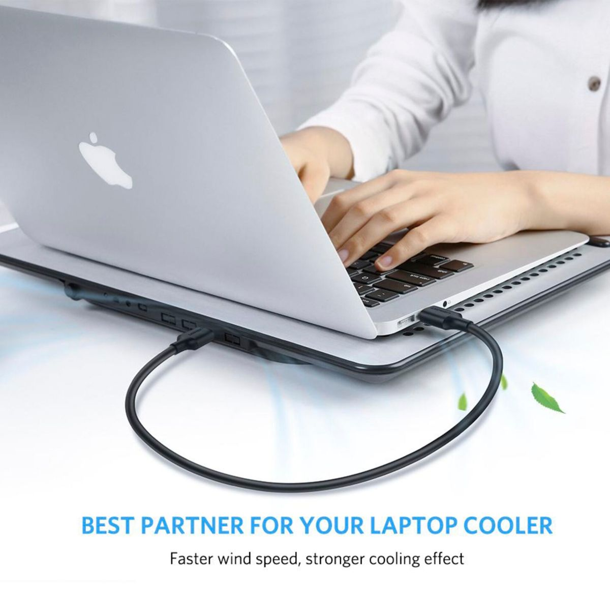 Laptop na podkładce chłodzącej. Ręka pisze. Kabel jest podłączony.