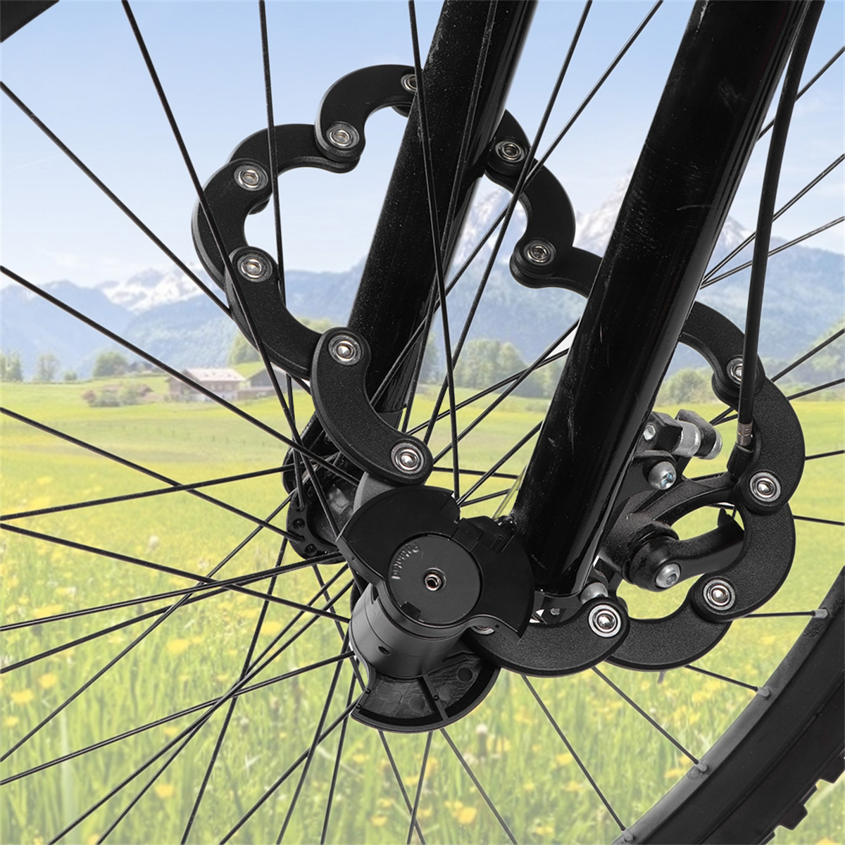 Schwarzes Fahrrad-Scheibenbremsenschloss an einem Rad mit grüner Wiese und Bergen im Hintergrund.