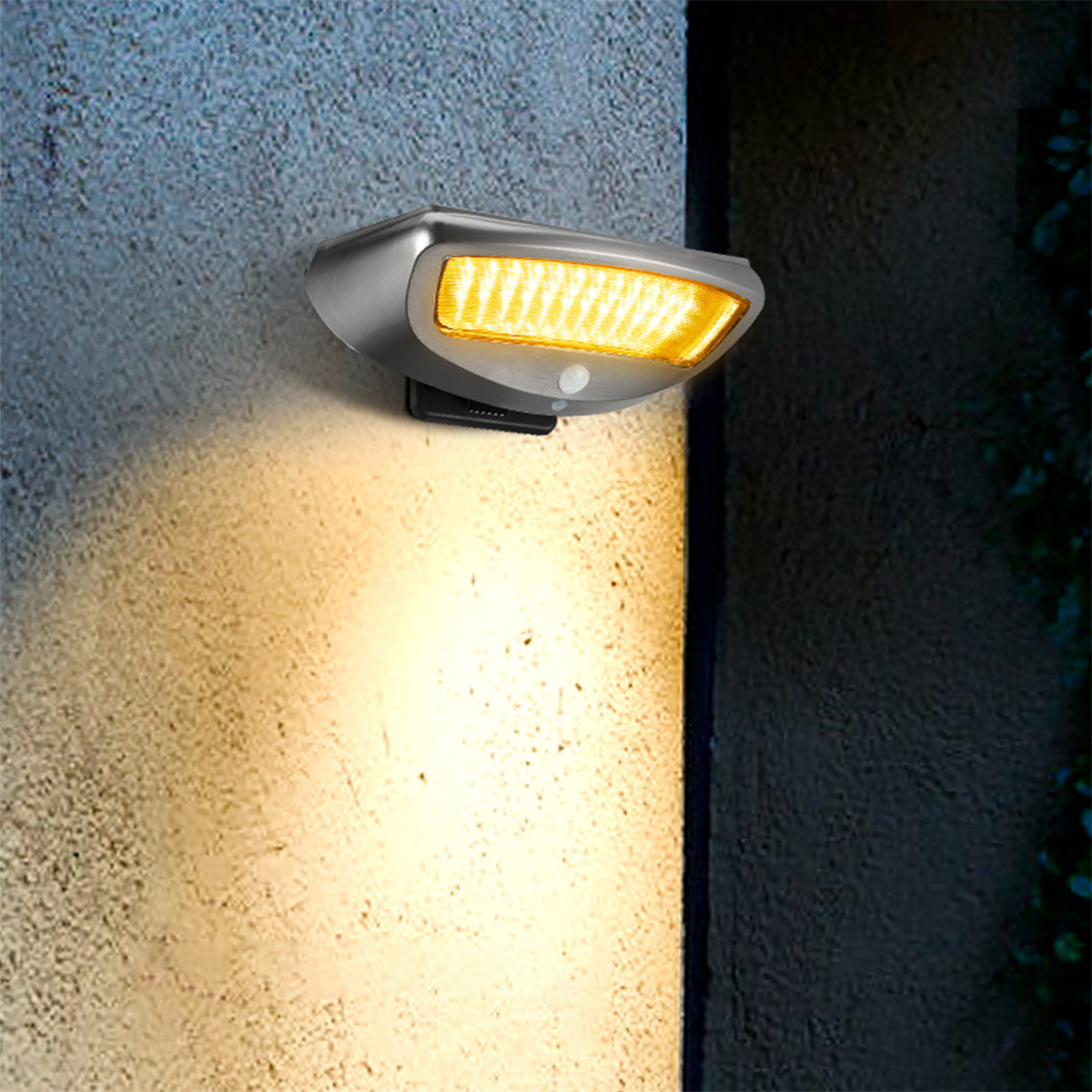 Eine silberne Outdoor-Bewegungsmelder-Leuchte an einer Wand, die gelbes Licht nach unten strahlt.