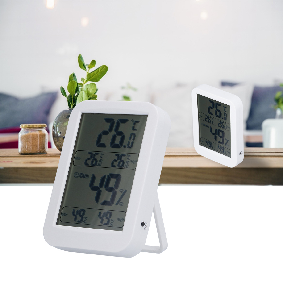 Zwei weiße digitale Thermometer zeigen Temperatur und Luftfeuchtigkeit an, eines auf einem Tisch, das andere abgewinkelt.