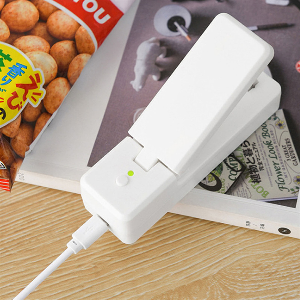 Weißes elektronisches Gerät mit USB-Kabel. Es liegt auf einer Zeitschrift mit fremdsprachigem Text.