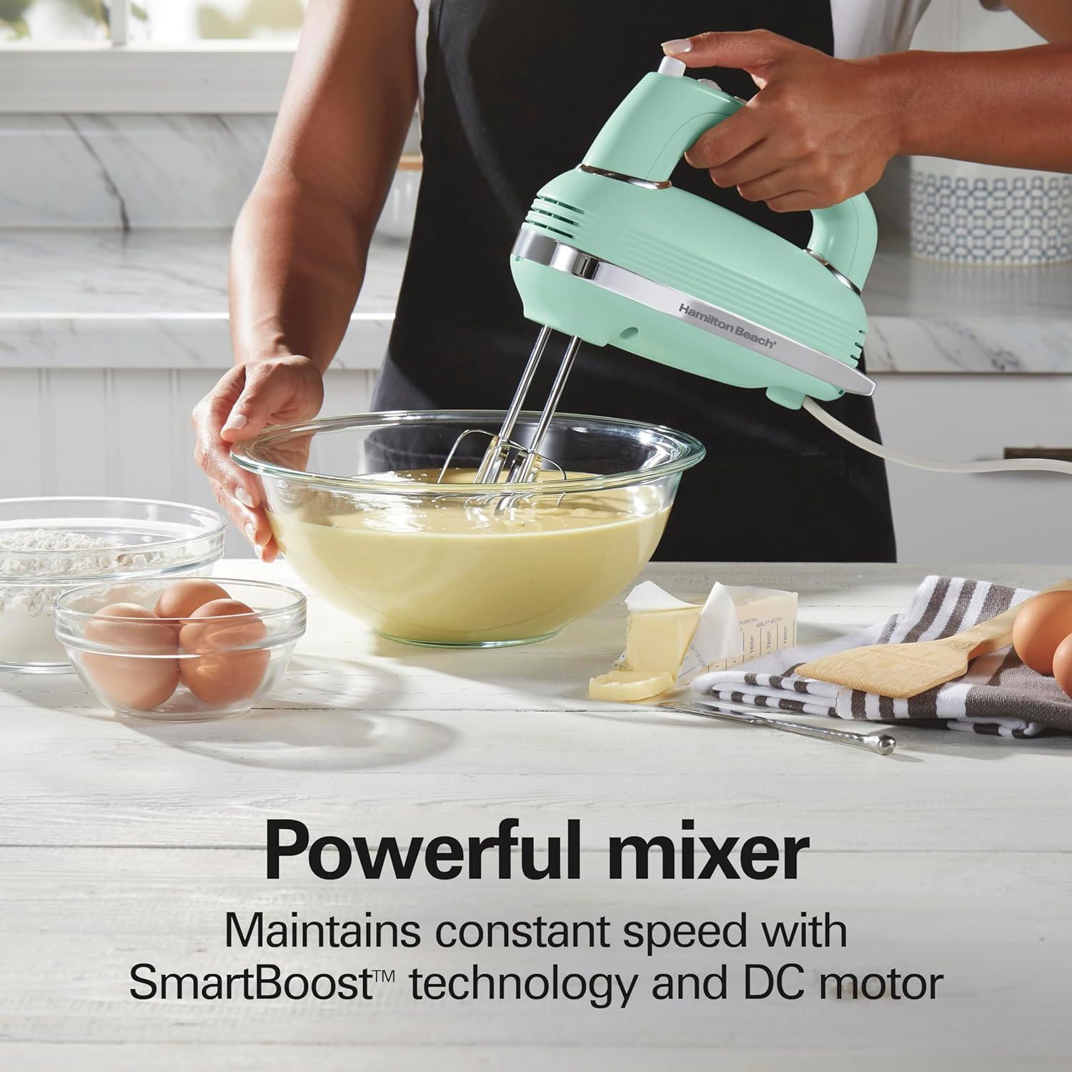 Eine Frau benutzt einen mintgrünen Handmixer. Zutaten im Vordergrund.