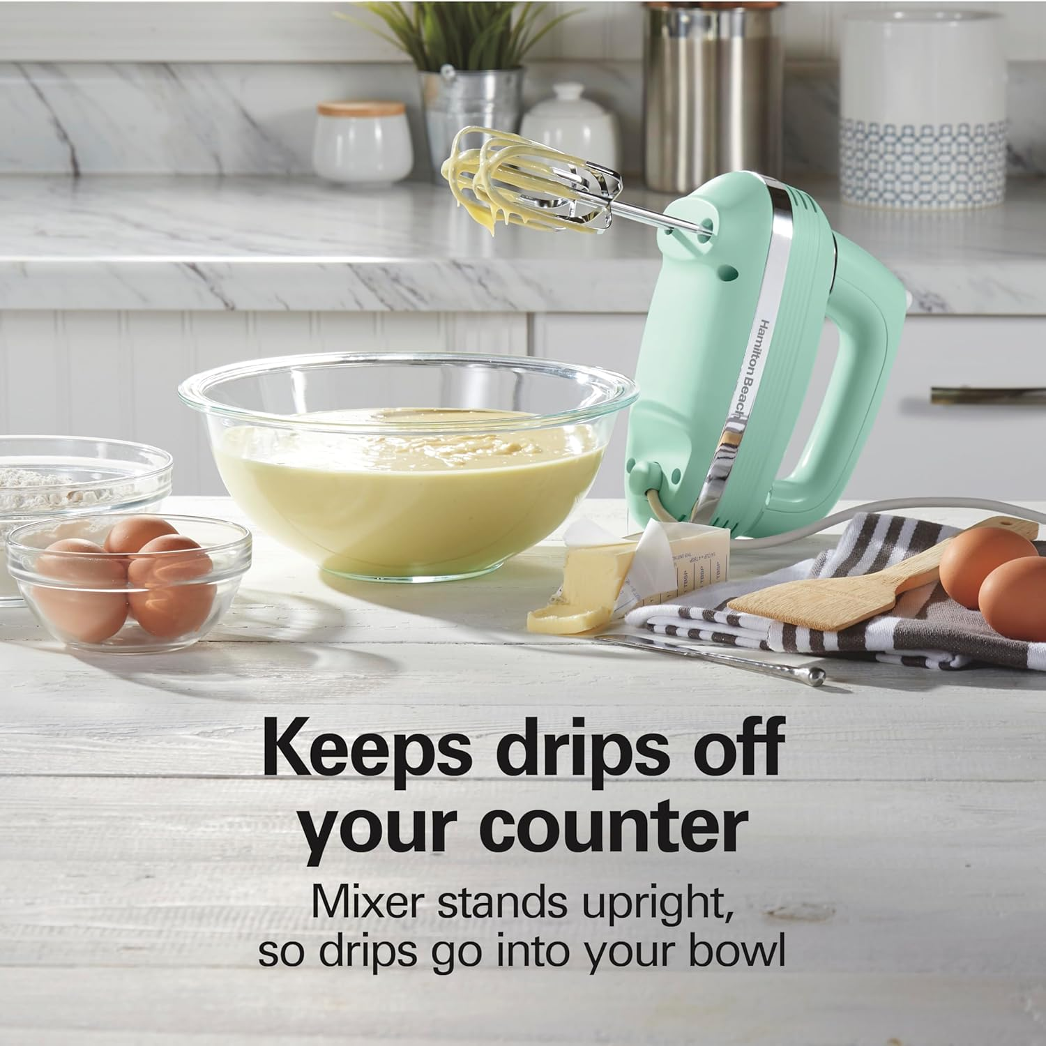 Ein grüner Handmixer wird mit Zutaten für einen Kuchen gezeigt. Der Mixer hält Tropfen von der Theke fern.