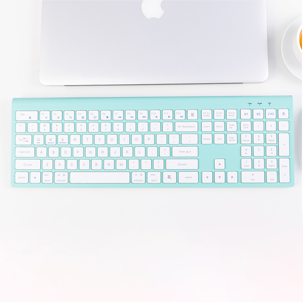 Jasnoniebieska klawiatura na białej powierzchni, nad nią srebrny laptop.