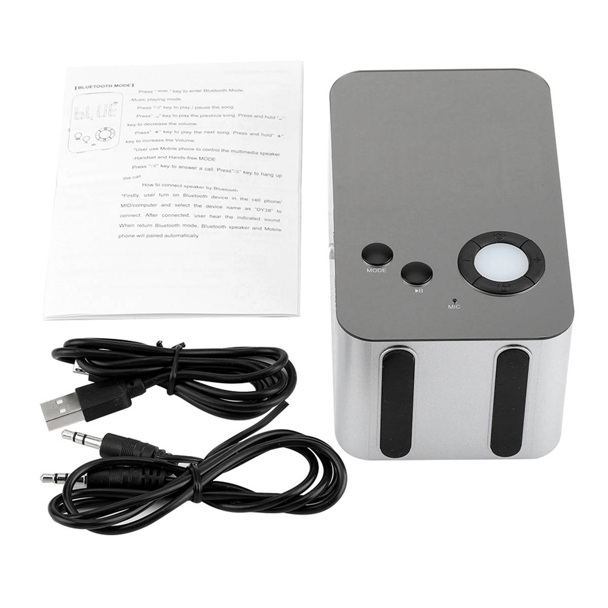 Ein silberner Bluetooth-Lautsprecher mit Bedienelementen, Kabeln und einer Bedienungsanleitung auf einer weißen Oberfläche.