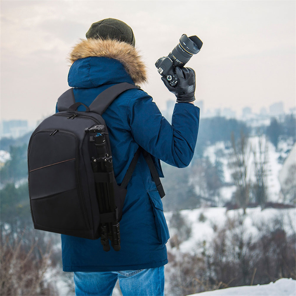 Ein Fotograf in einer blauen Jacke mit Rucksack und Stativ, der eine Kamera hält.