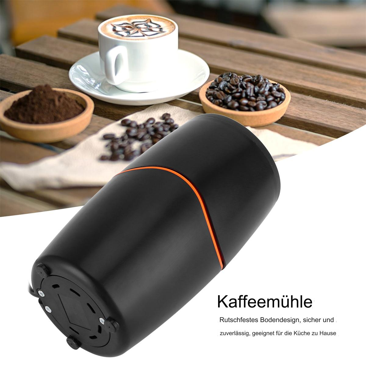 Schwarze Kaffeemühle mit orangefarbenen Akzenten. Kaffeepulver, Bohnen und eine Tasse Kaffee auf einem Holztisch.