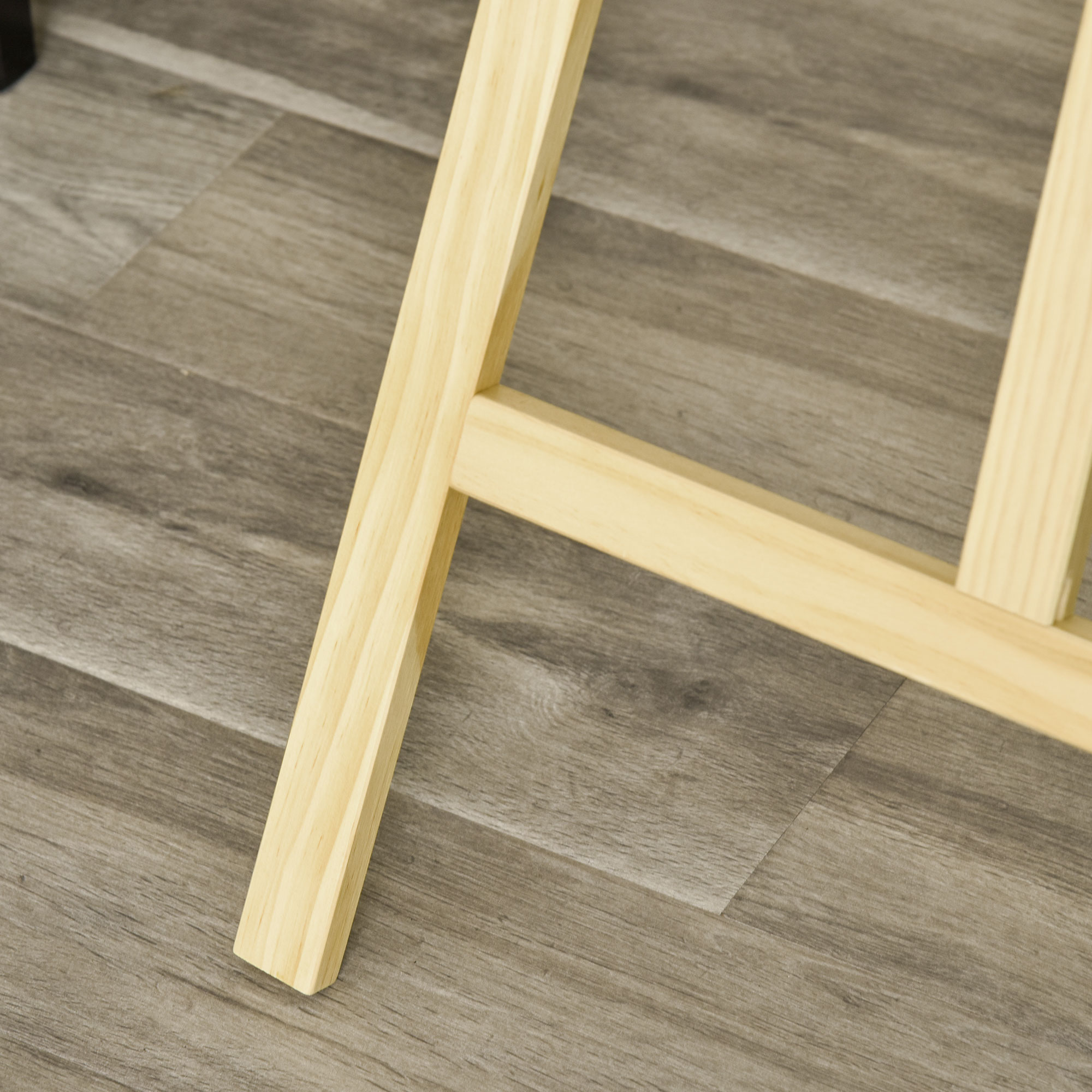 Primer plano de una pata de caballete de madera sobre un suelo de madera gris. La pata está en ángulo.